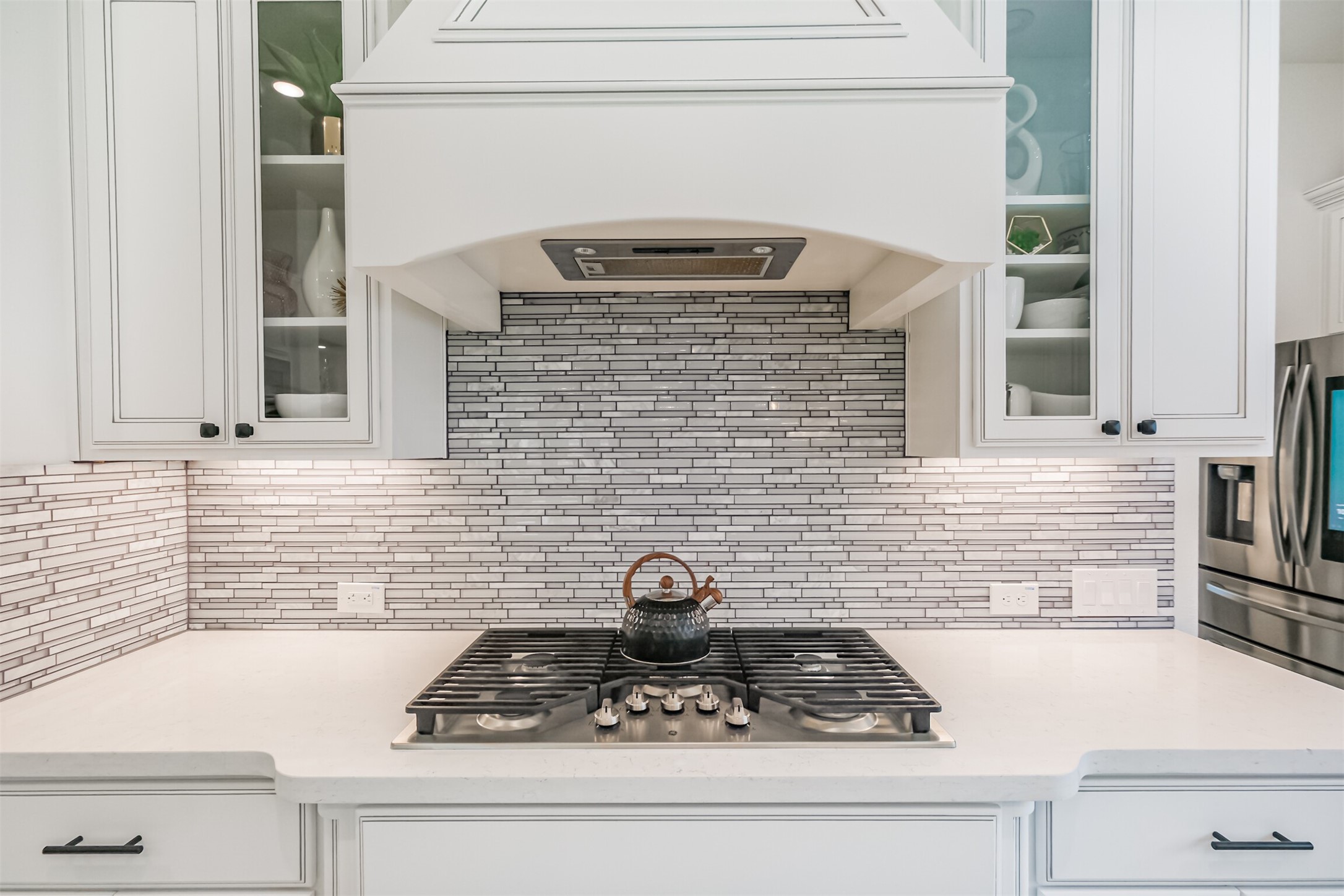 Luxuriously appointed kitchen featuring custom Benedettini cabinetry with elegant glass-front display cabinets, a sleek GE gas cooktop, and a sophisticated mosaic glass backsplash.