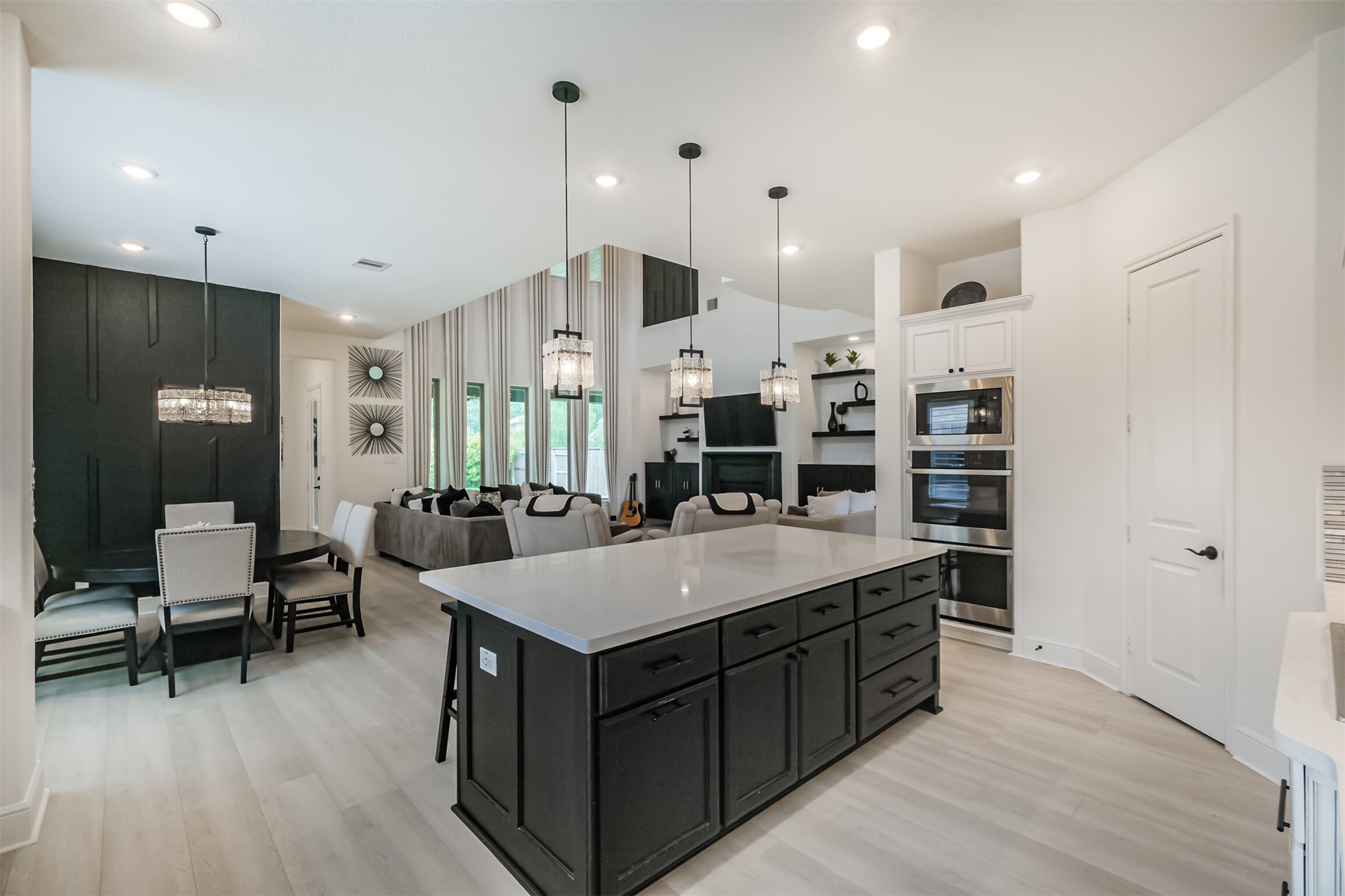 Luxurious open-concept kitchen designed for both elegant entertaining and everyday living, featuring an expansive center island, sophisticated pendant lighting, double ovens, built-in microwave, and refined finishes throughout. The kitchen flows seamlessly into the dining and living areas, where a custom accent wall adds a distinctive designer touch.