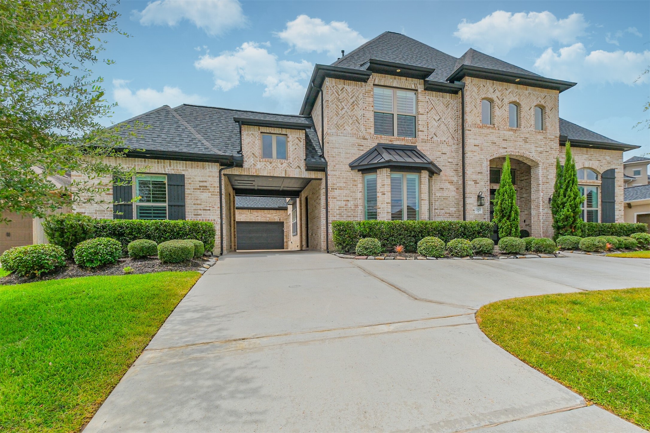 Stunning two-story brick home with elegant architectural details, manicured landscaping, and a spacious 'U' driveway leading to a charming porte-cochre.