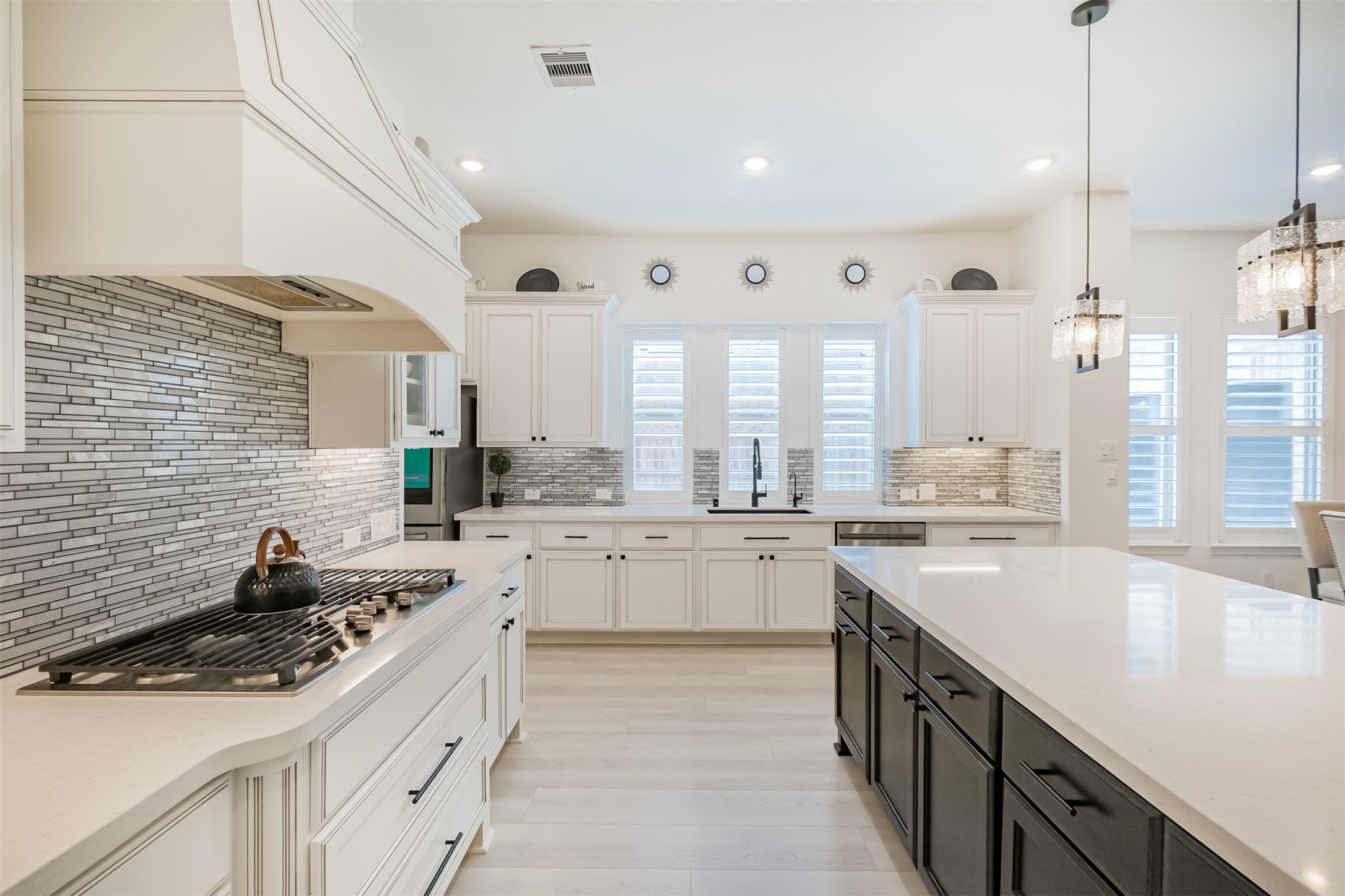 This luxuriously appointed kitchen showcases custom Benedettini cabinetry, rich granite countertops, and an elegant glass mosaic tile backsplash. Designed with both beauty and functionality in mind, it features a high-end gas cooktop, GE appliances, two dedicated pots-and-pans drawers, and dual built-in trash compartments for a seamless, sophisticated finish.