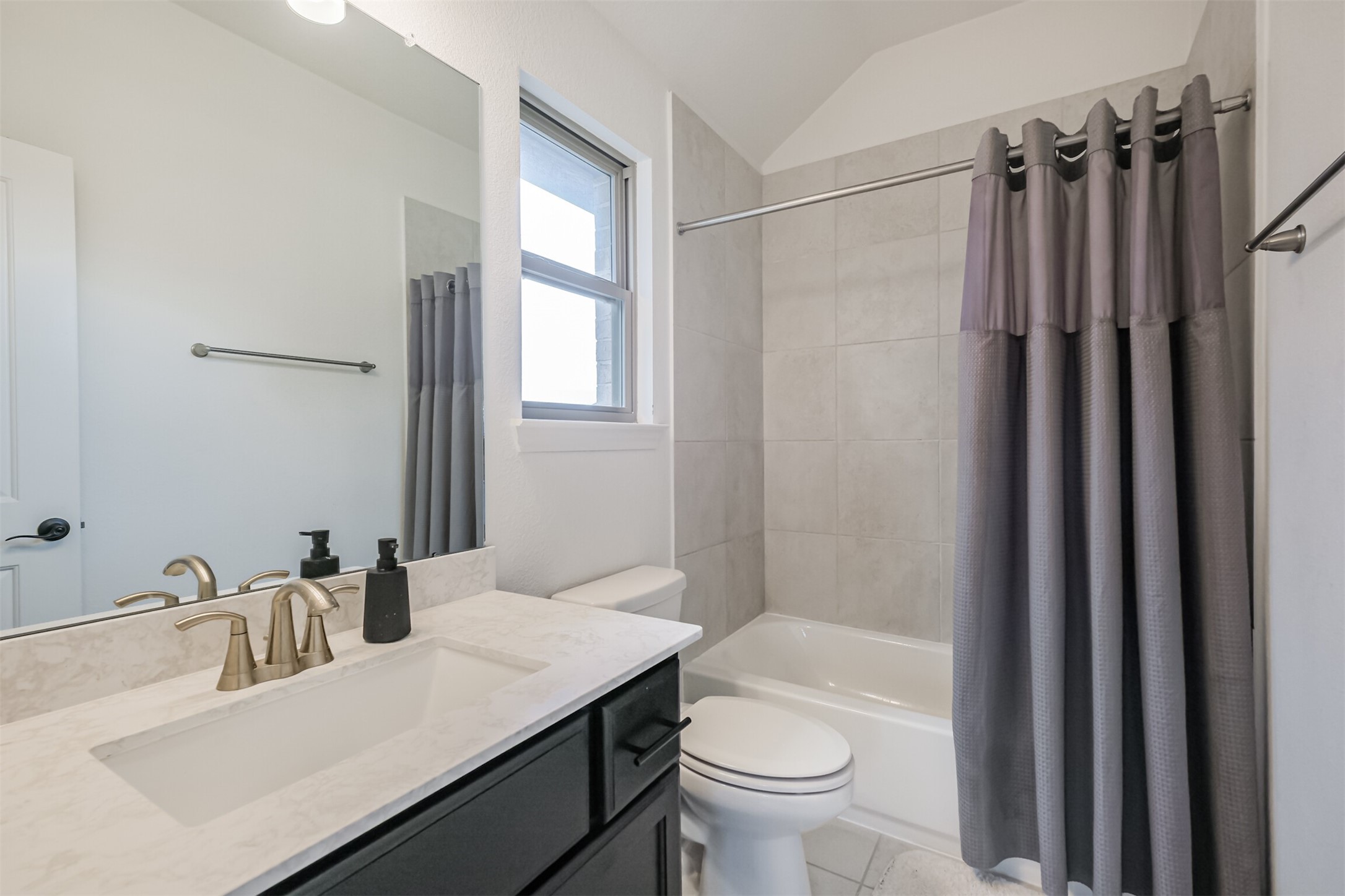 Sophisticated second primary bathroom featuring a sleek contemporary vanity accented with elegant brass fixtures, an expansive mirror, and a beautifully tiled shower-tub combination, creating a polished and inviting private retreat.