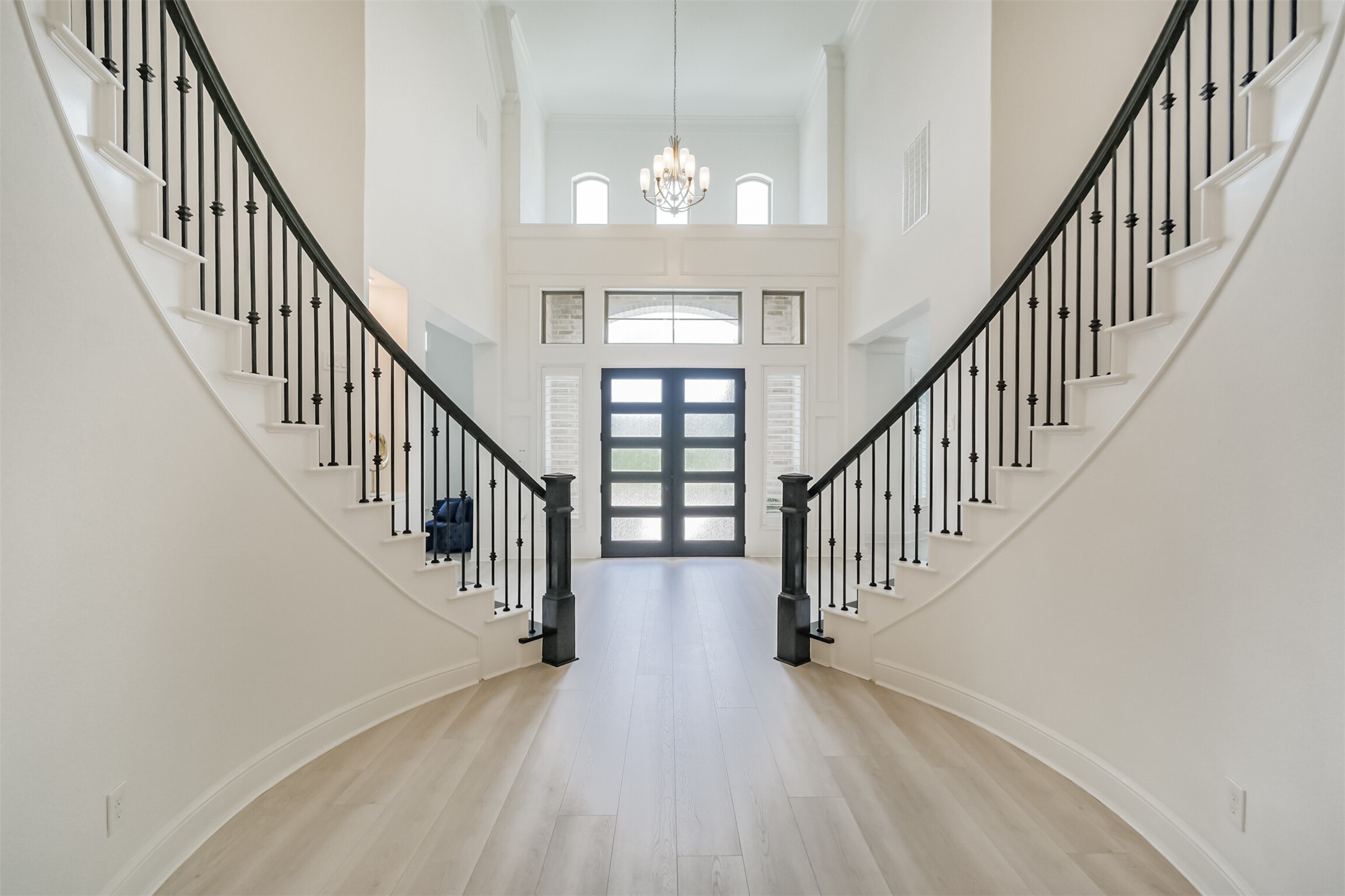 Another view of the grand foyer, showcasing dramatic dual sweeping staircases, soaring ceilings, and rich engineered hardwood flooringcreating a refined and impressive entrance that sets the tone for the home.