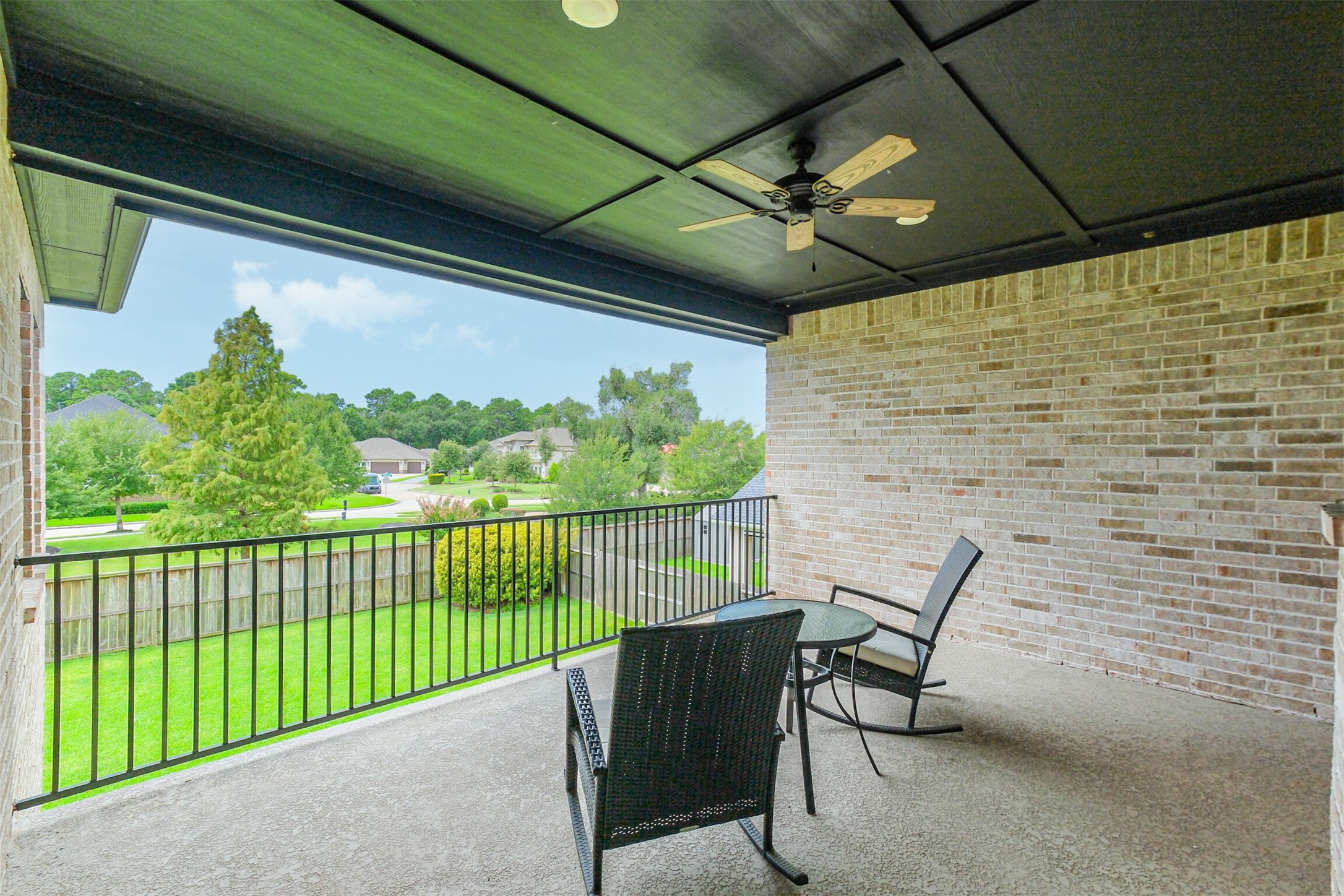 Another view of the expansive second-floor covered balcony, featuring a ceiling fan and generous space for outdoor seating. Overlooking the lush backyard and surrounding neighborhood, this elevated retreat provides a serene setting for relaxing and enjoying the views.