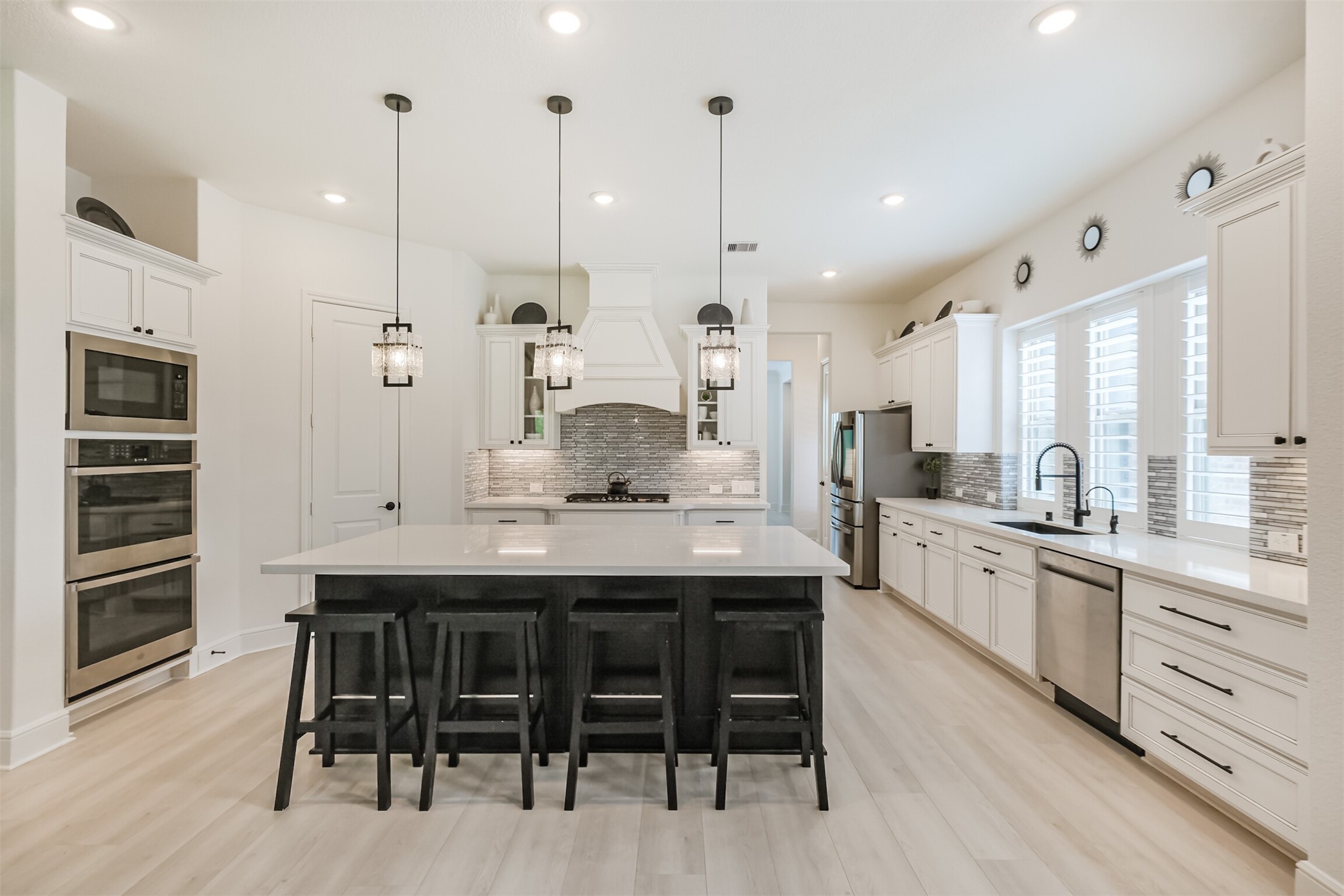 A beautifully appointed kitchen designed with both luxury and functionality in mind, featuring an expansive center island with seating, stainless steel appliances, and sophisticated pendant lighting. Thoughtful upgrades include crown molding, soft-close cabinetry and drawers throughout, a generous walk-in pantry, and elevated 8-foot plank wood-look water-resistant flooring, creating a polished and timeless space ideal for everyday living and entertaining.