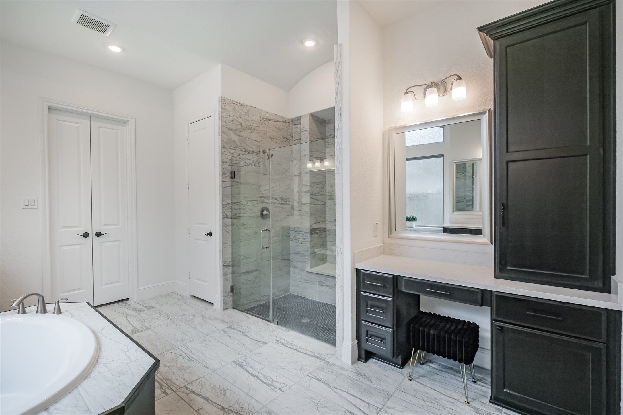 Spa-inspired primary bathroom featuring an expansive glass-enclosed walk-in shower, luxurious soaking tub, and elegant marble tile flooring. A dedicated private vanity area and generous storage add both function and sophistication, creating a serene, resort-like retreat.