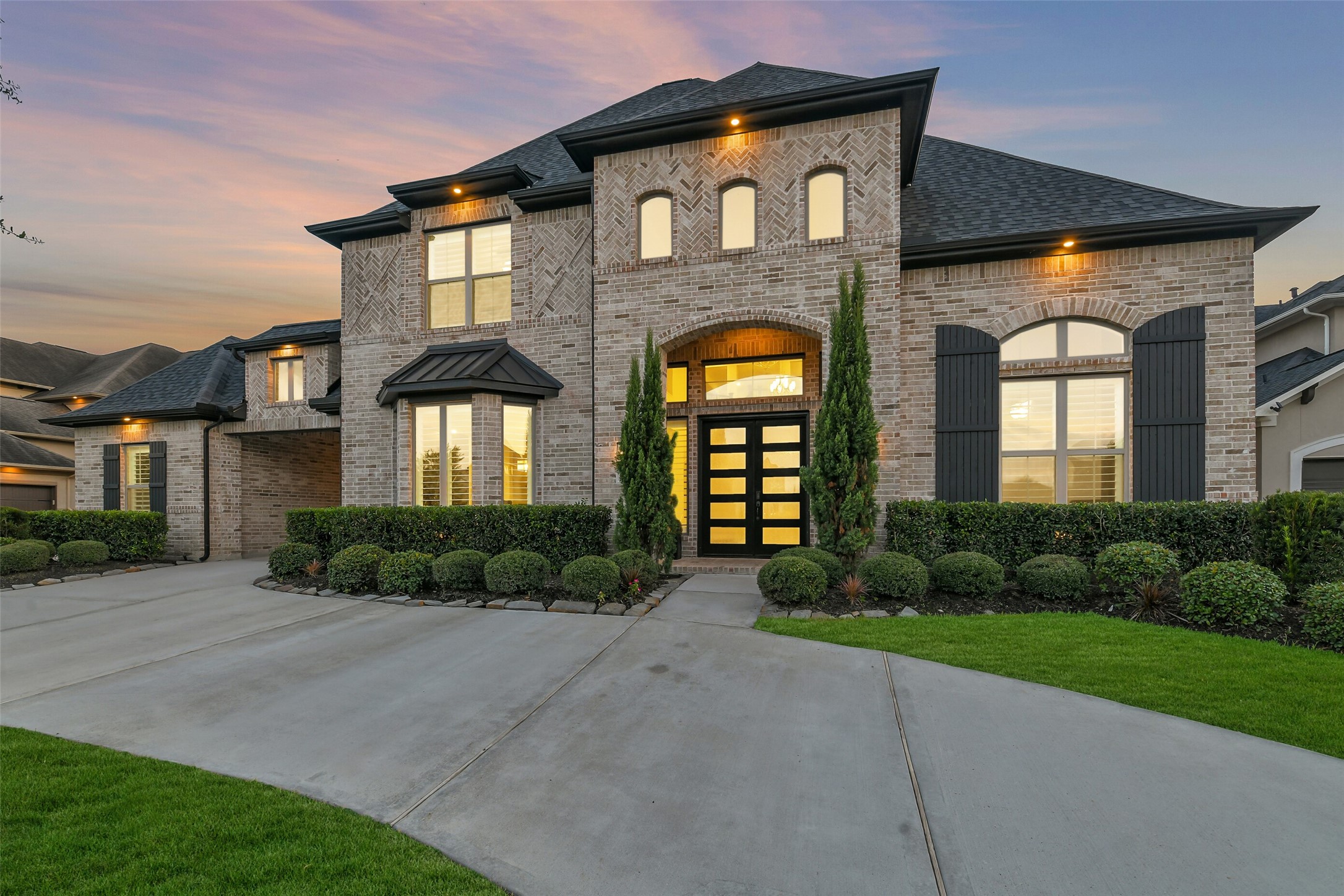 Elegant two-story brick home featuring a spacious curved driveway, beautifully manicured landscaping, and striking black shutters. The roof is less than three years old, adding to the homes impressive curb appeal and value.