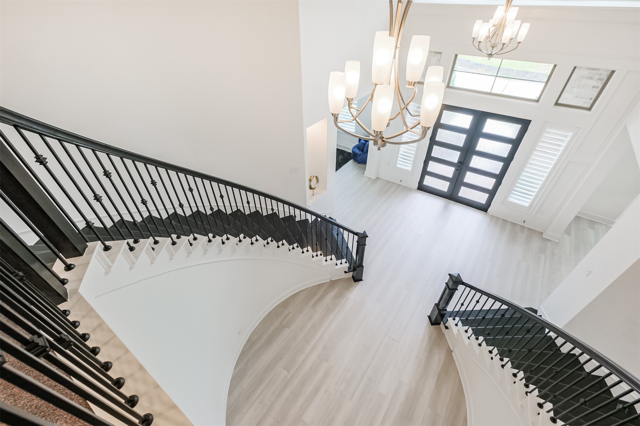Grand foyer with a sweeping dual staircase, modern chandelier, and elegant double doors, exuding luxury and sophistication.