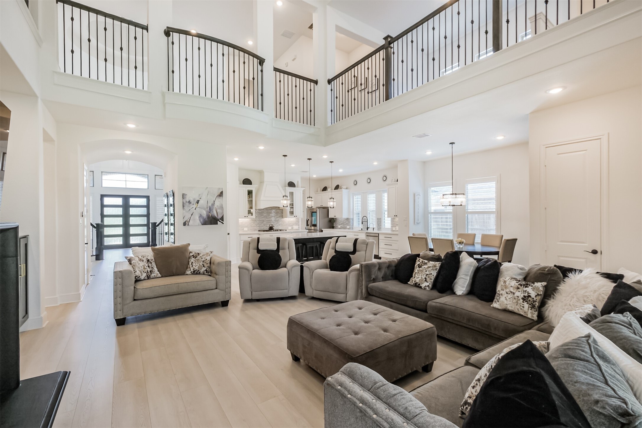 Expansive and elegant living area featuring soaring ceilings and a dramatic second-story balcony overlooking the space below. The thoughtfully designed open-concept layout flows seamlessly into the gourmet kitchen, creating an impressive setting for both everyday living and entertaining.