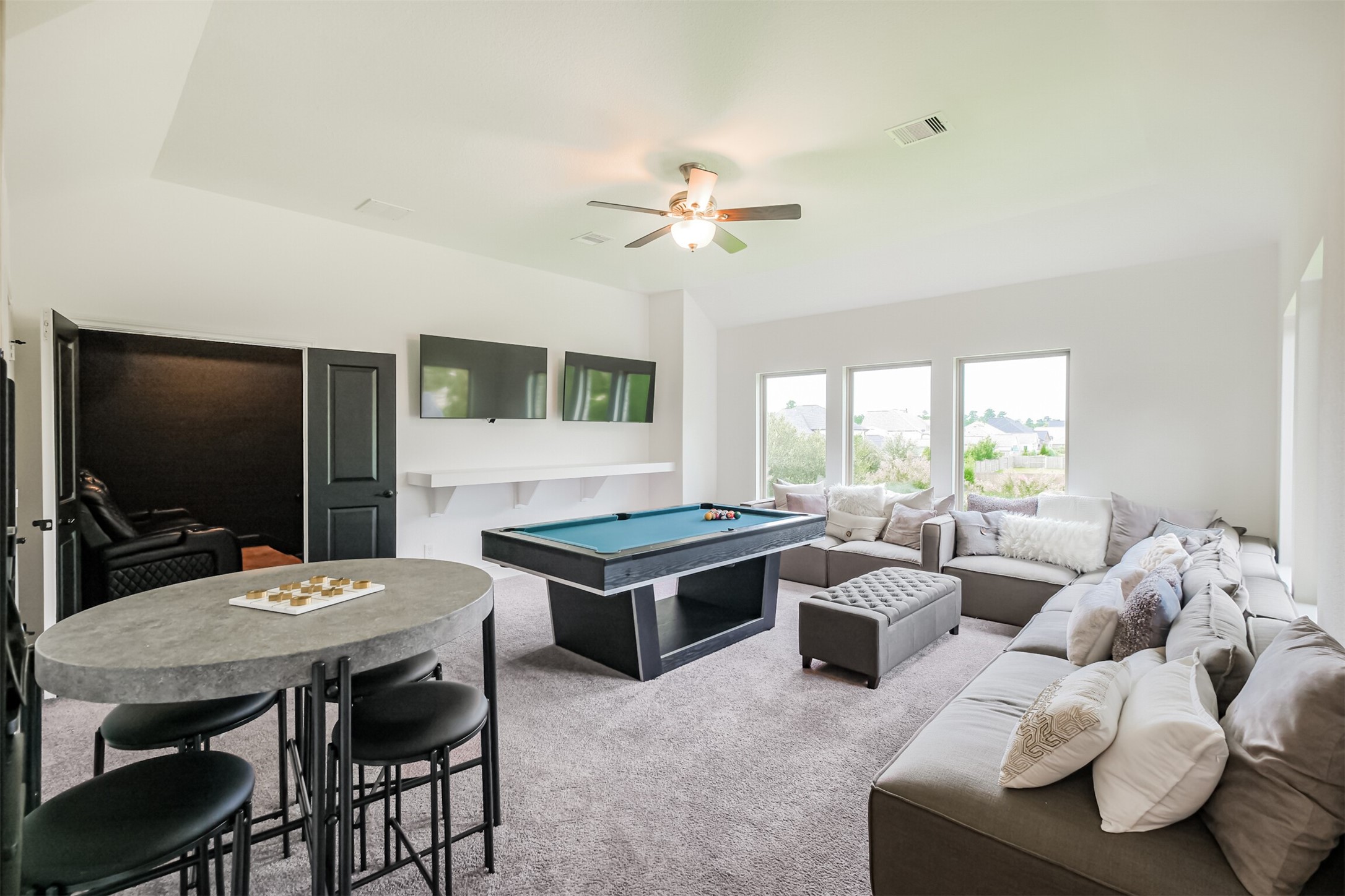 Expansive entertainment and game room designed for memorable gatherings, featuring generous seating areas, a built-in bar counter, and oversized windows that fill the space with natural light. With abundant room for hosting family and friends, plus a dedicated media room and convenient half bath just off the game room, this impressive retreat delivers the ultimate setting for elevated at-home entertainment.