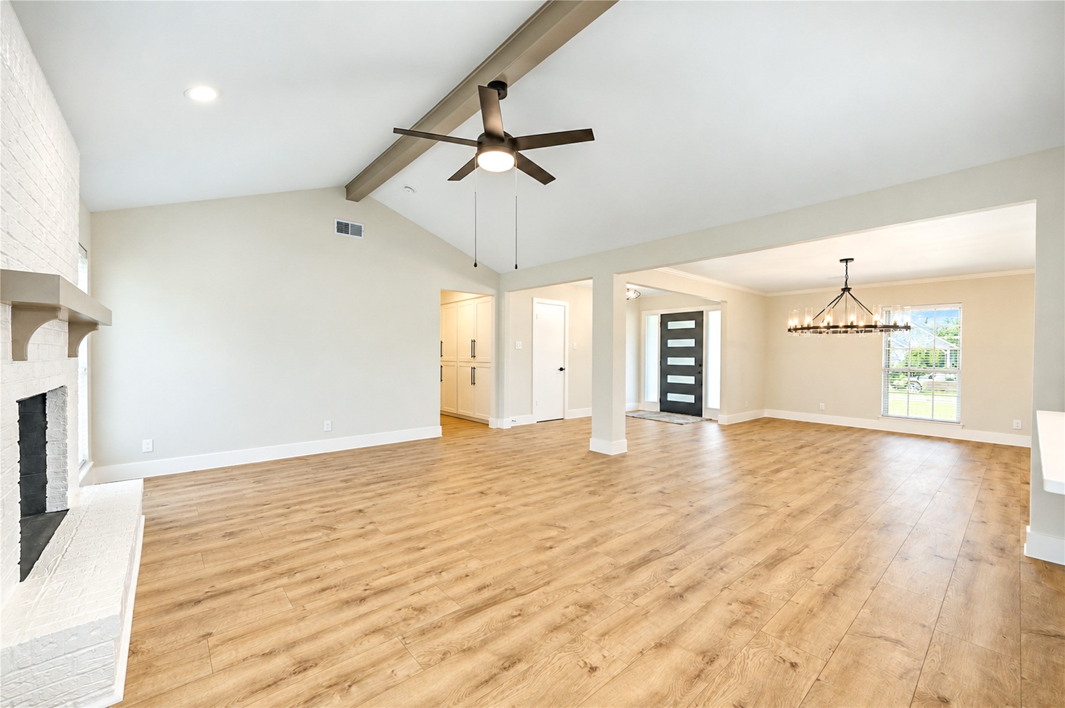 Another view of the spacious family room featuring a vaulted ceiling, decorative wood beam, contemporary ceiling fan, and new wide-plank engineered wood flooring.