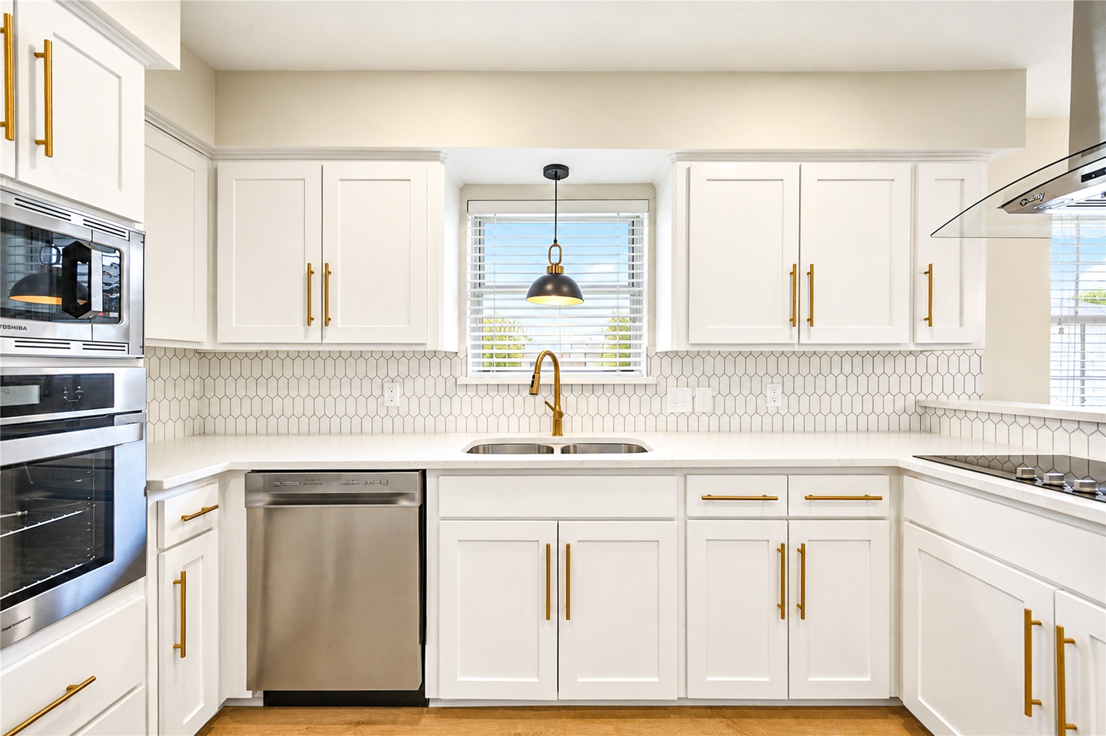Beautifully remodeled kitchen showcases all-new stainless steel appliances, including built-in oven and microwave, elegant Shaker-style cabinetry with soft-close doors, gold hardware, and a designer tile backsplash.