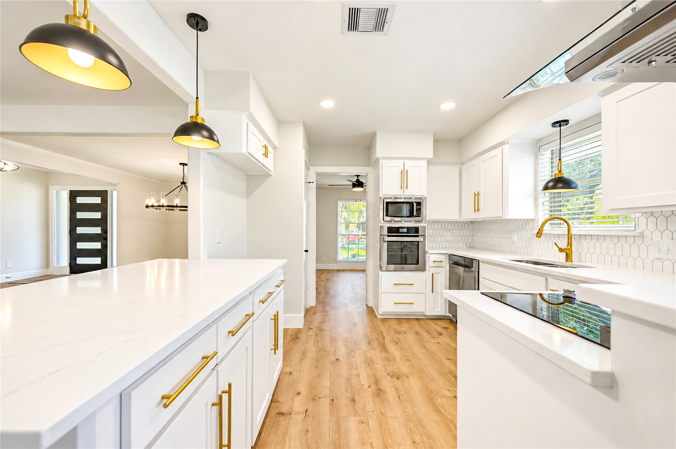 Stunning remodeled kitchen opens seamlessly to the family room and features a breakfast bar with seating for barstools, white cabinetry, quartz countertops, designer backsplash, stainless steel appliances, elegant gold accents, and all-new designer lighting.