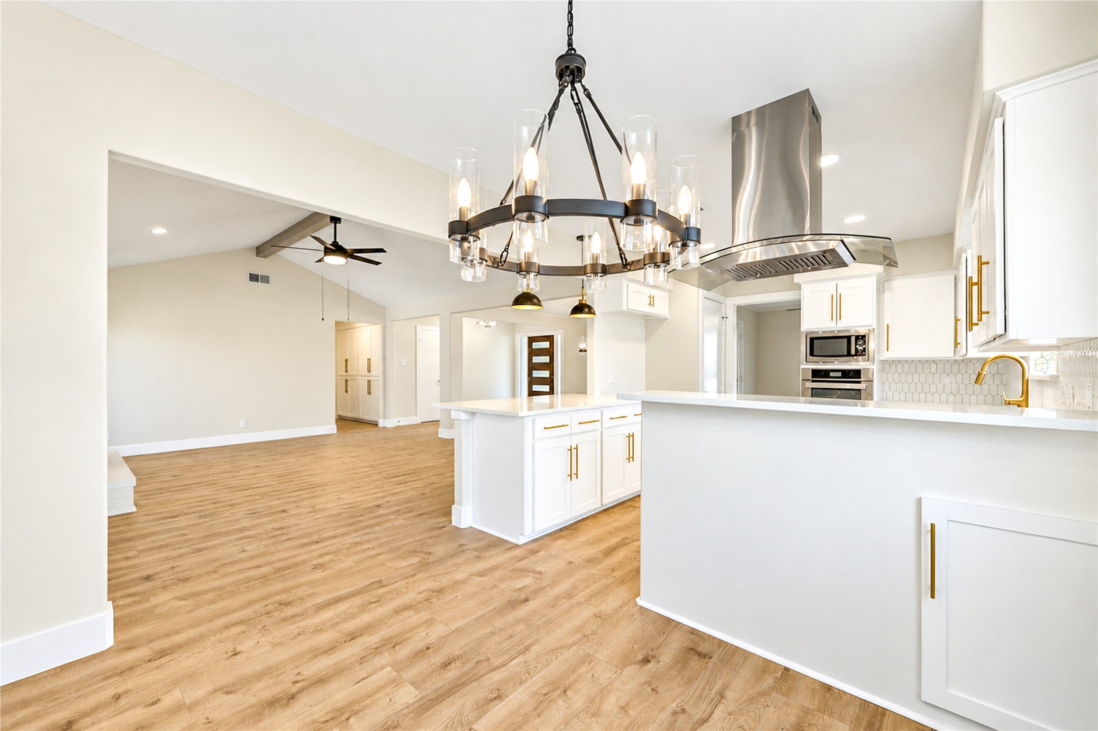 Thoughtfully remodeled kitchen opens to the dining and living areas, featuring elegant white cabinetry, gold hardware, designer lighting, and generous counter space.