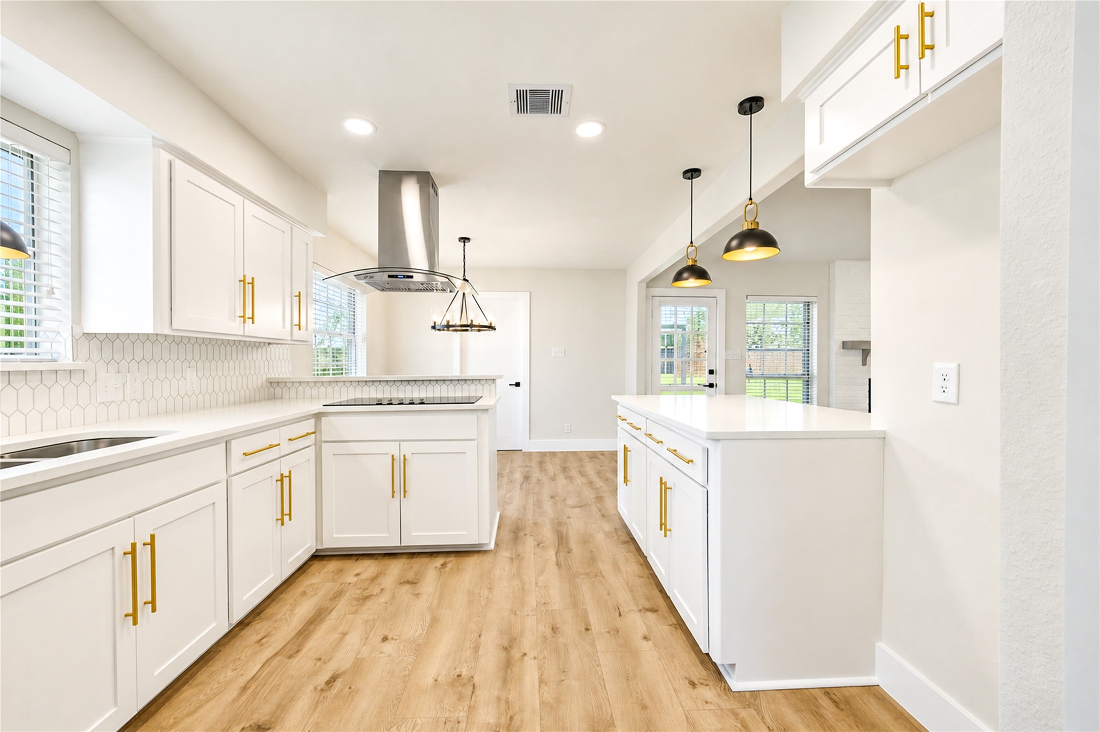 Another view of the beautifully remodeled kitchen highlights its functional layout, abundant shaker-style cabinetry, recessed lighting, and new wide-plank engineered wood flooring.