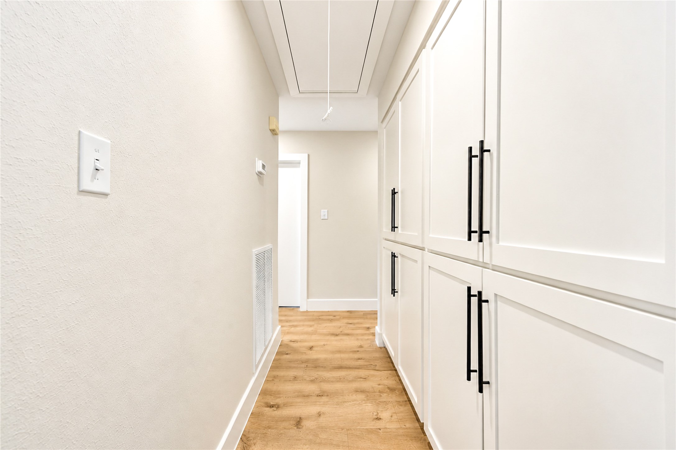 Impressive hallway features an entire wall of built-in storage cabinetry with all-new Shaker-style door fronts, providing exceptional storage and organization throughout the home.