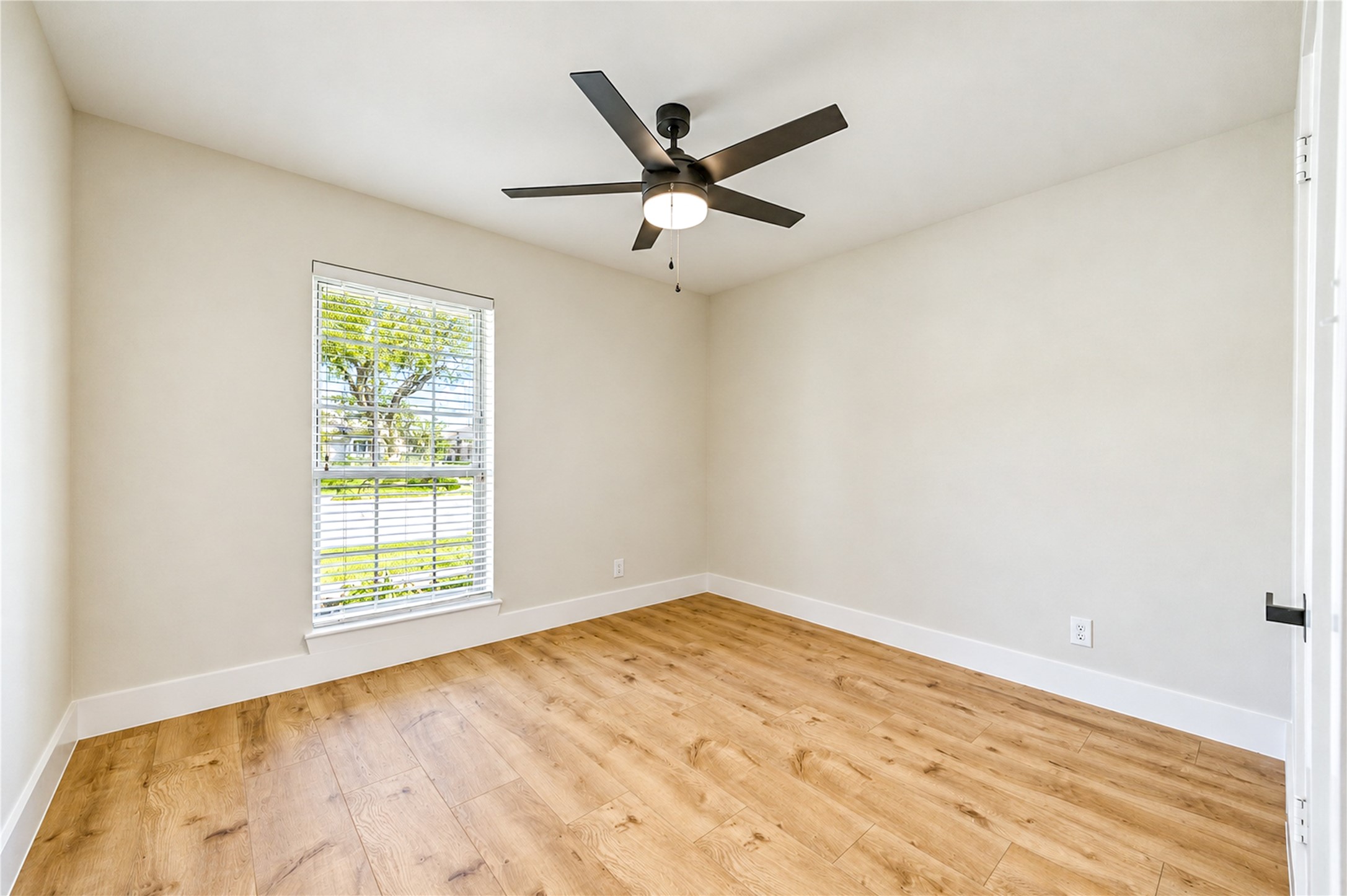Bright and inviting secondary bedroom features new wide-plank engineered wood flooring, a contemporary ceiling fan, fresh neutral finishes, and abundant natural light.