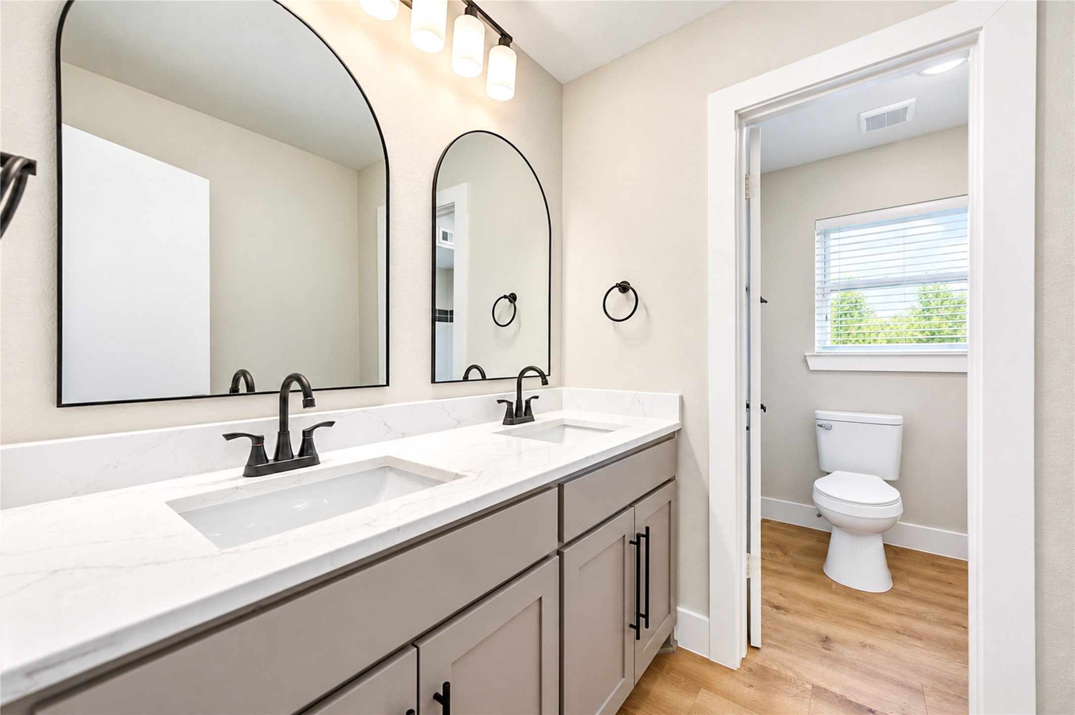 Beautifully remodeled secondary bathroom features a spacious dual-sink vanity with all-new Shaker-style cabinetry and soft-close doors, elegant arched mirrors, new faucets, designer lighting, and stylish contemporary finishes.