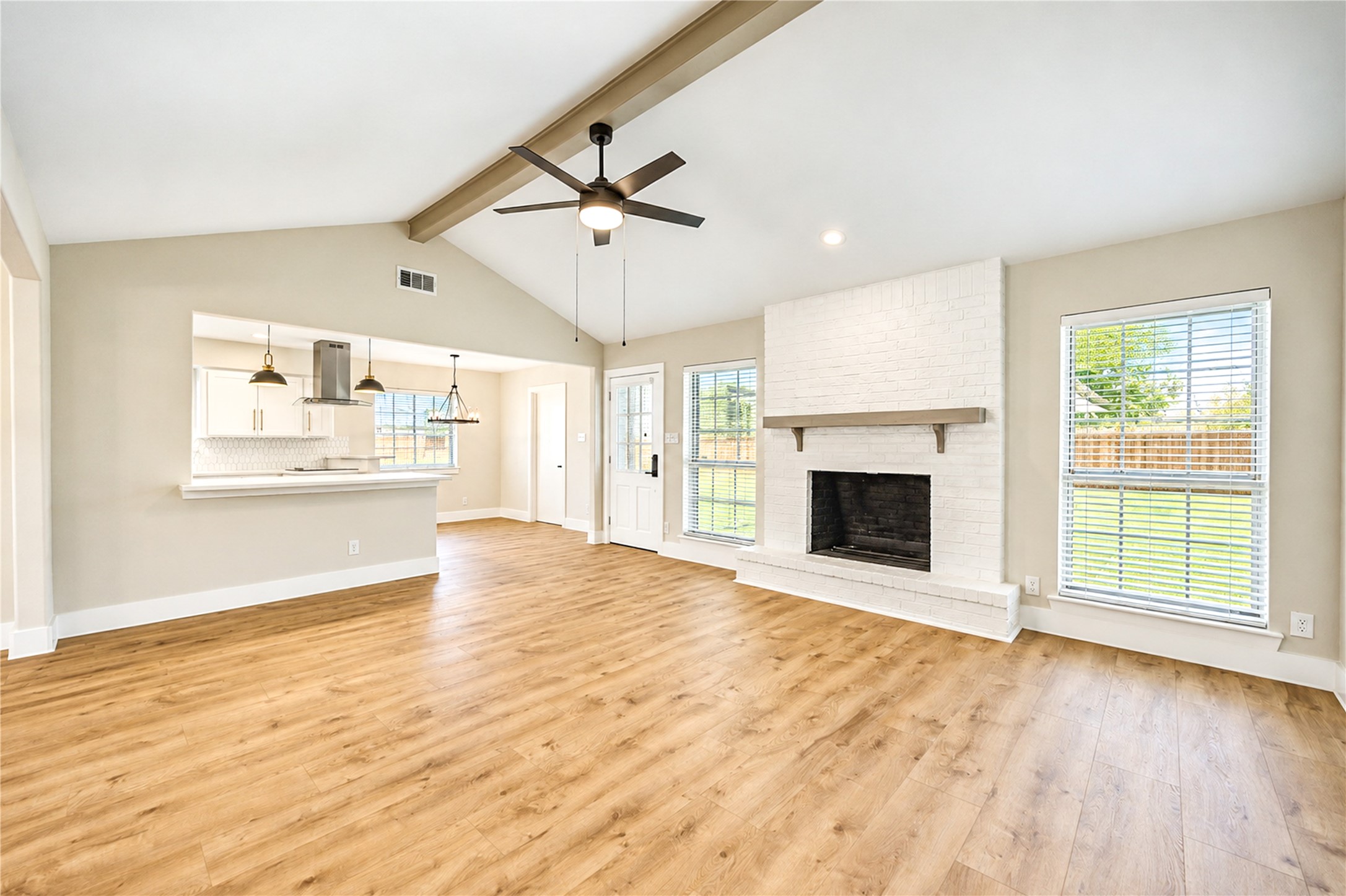 Spacious family room features vaulted ceilings, decorative wood beam, stylish fireplace, new ceiling fan, and gorgeous wide-plank engineered wood flooring.