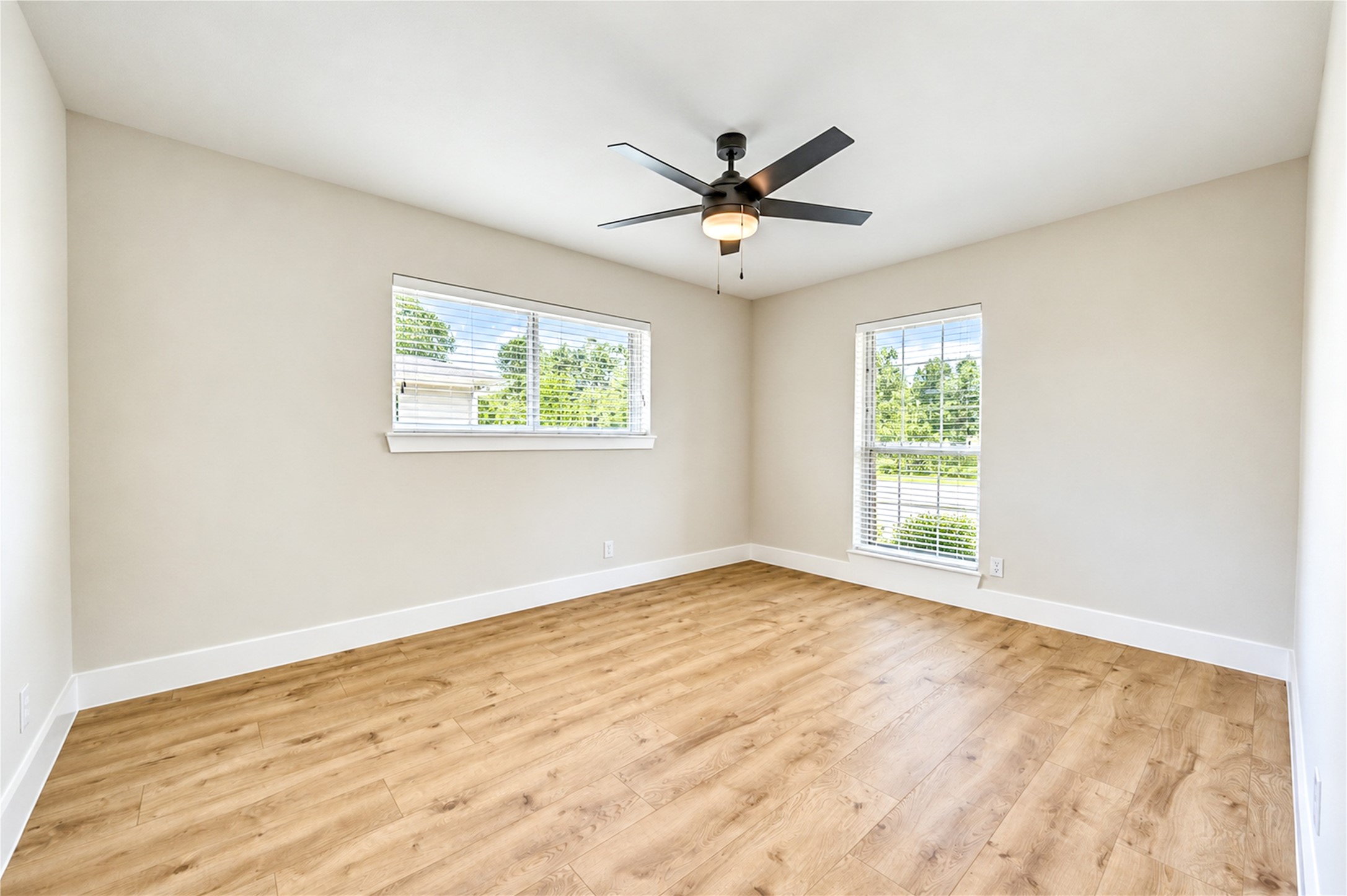 Spacious secondary bedroom showcases beautiful new engineered wood flooring, a new ceiling fan, large windows, and updated Shaker-style baseboards and door casings.
