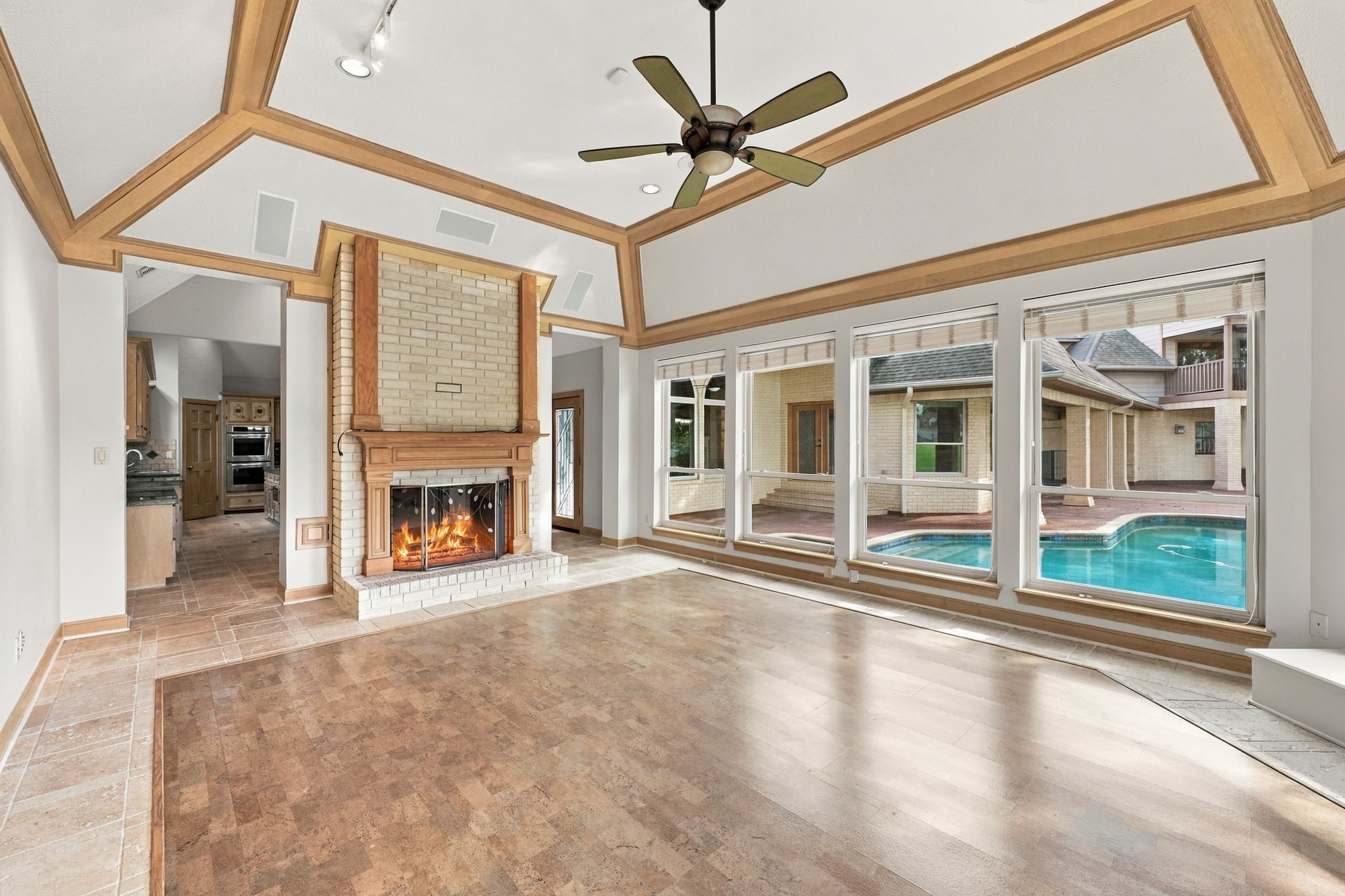 Looking from the opposite side of the room toward the Kitchen, you'll appreciate the beautiful double-sided fireplace that adds warmth and ambiance to both adjoining living spaces. The unique bamboo flooring, accented by surrounding tile, adds character and warmth, while the view extends toward the sparkling pool and spa, creating another wonderful vantage point of the home's resort-style backyard.