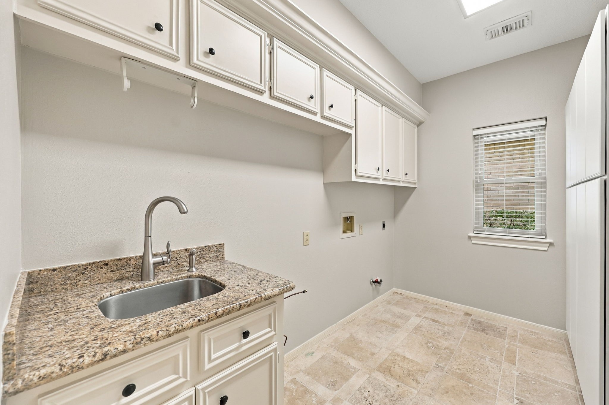 The spacious Laundry Room is thoughtfully designed with a built-in sink, granite countertop, and brushed nickel gooseneck faucet. Abundant built-in shelving provides plenty of storage and organization, making everyday tasks a little easier.