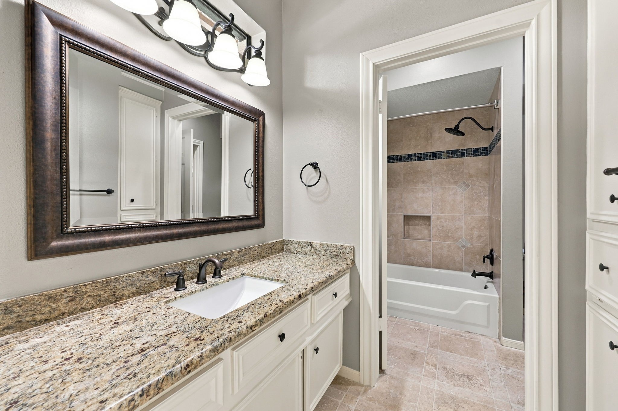 This side of the Jack-and-Jill Bathroom serves the bedroom featured in the previous photos and offers light cabinetry, granite countertops, an undermount sink, a framed mirror, and an oil-rubbed bronze widespread faucet. A tub and shower combination completes this well-appointed space.