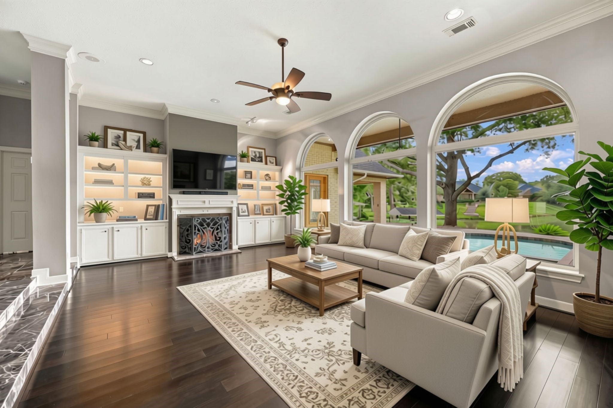 The spacious Family Room features impressive 12-foot ceilings, beautiful wood-look luxury vinyl plank flooring, and three large arched windows that frame gorgeous views of the resort-style backyard and waterfront setting. A gas-log fireplace serves as the focal point, flanked by custom built-in shelving with accent lighting on either side. This inviting space offers the perfect setting for relaxing, gathering, and enjoying the home's beautiful surroundings. (VIRTUALLY STAGED)
