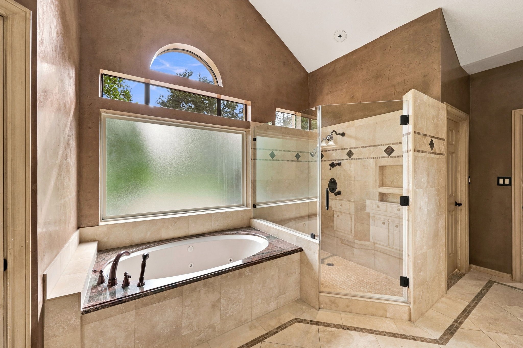 The spacious jetted soaking tub is beautifully positioned beneath a privacy glass window, allowing natural light while maintaining privacy. Featuring an elegant granite and tile surround with coordinating oil-rubbed bronze fixtures, this inviting space is perfect for relaxing and unwinding.