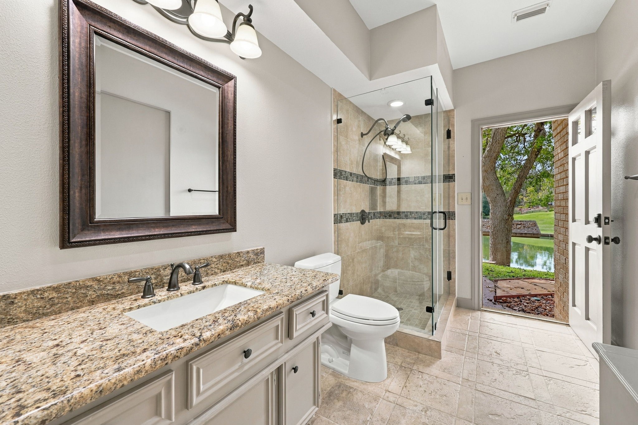 The main home offers three Full Bathrooms, including this conveniently located Full Bath with direct access to the backyard, making it ideal for use as a pool bath. Features include light cabinetry, granite countertops, an undermount sink, a framed mirror, and an oil-rubbed bronze widespread faucet. A walk-in shower with a frameless glass enclosure completes this well-appointed space.