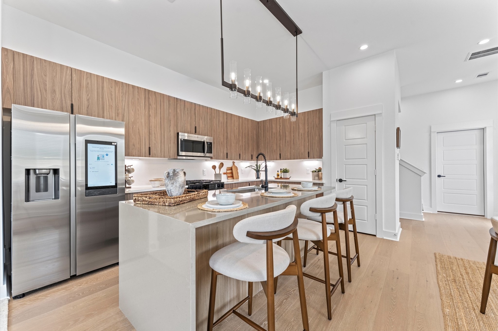 This stunning kitchen island is the centerpiece of a modern open-concept layout, featuring a waterfall quartz countertop that cascades elegantly down one side for high-end look. Positioned to offer clear sightlines to the living and dining areas, as well as through French doors to the balcony, the island enhances both functionality and flow. Contemporary finishessuch as sleek cabinetry, bold pendant lighting, and integrated appliancesadd sophistication, while bar seating invites casual dining.