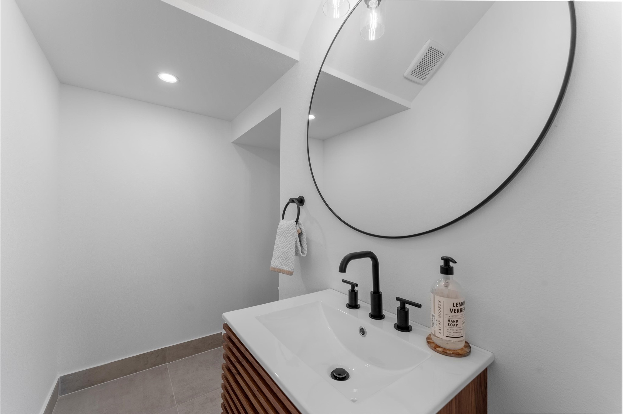 This stylish second-floor powder room blends modern elegance with functional design. Featuring contemporary finishes throughout, the space includes a sleek vanity with clean lines and minimalist hardware. The vanity is paired with a statement mirror and bold lighting fixtures that add visual interest.