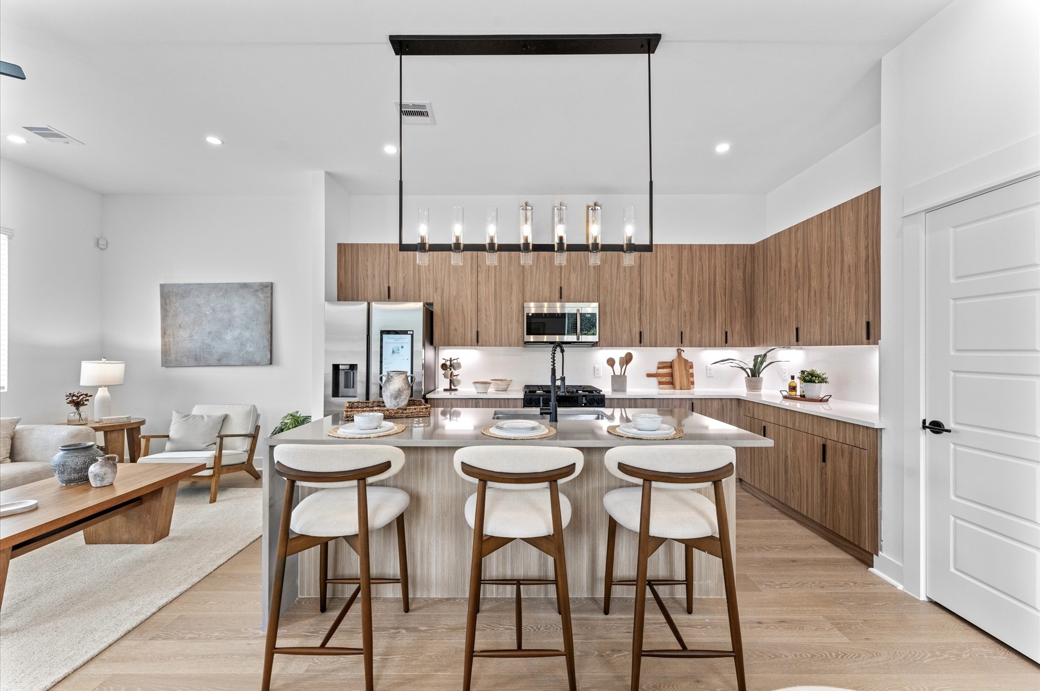 This stunning kitchen island is the centerpiece of a modern open-concept layout, featuring a waterfall quartz countertop that cascades elegantly down one side for high-end look. Positioned to offer clear sightlines to the living and dining areas, as well as through French doors to the balcony, the island enhances both functionality and flow. Contemporary finishessuch as sleek cabinetry, bold pendant lighting, and integrated appliancesadd sophistication, while bar seating invites casual dining.