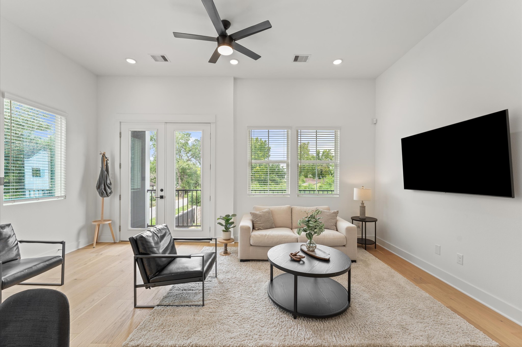 Airy and inviting open-concept living space located on the second floor, thoughtfully designed to enhance both comfort and flow. The area features high ceilings, expansive windows, and cohesive flooring that unify the living, dining, and kitchen zones. Elegant French doors serve as a striking focal point, leading out to a private balcony that extends the living space outdoorsperfect for morning coffee or evening unwinding.