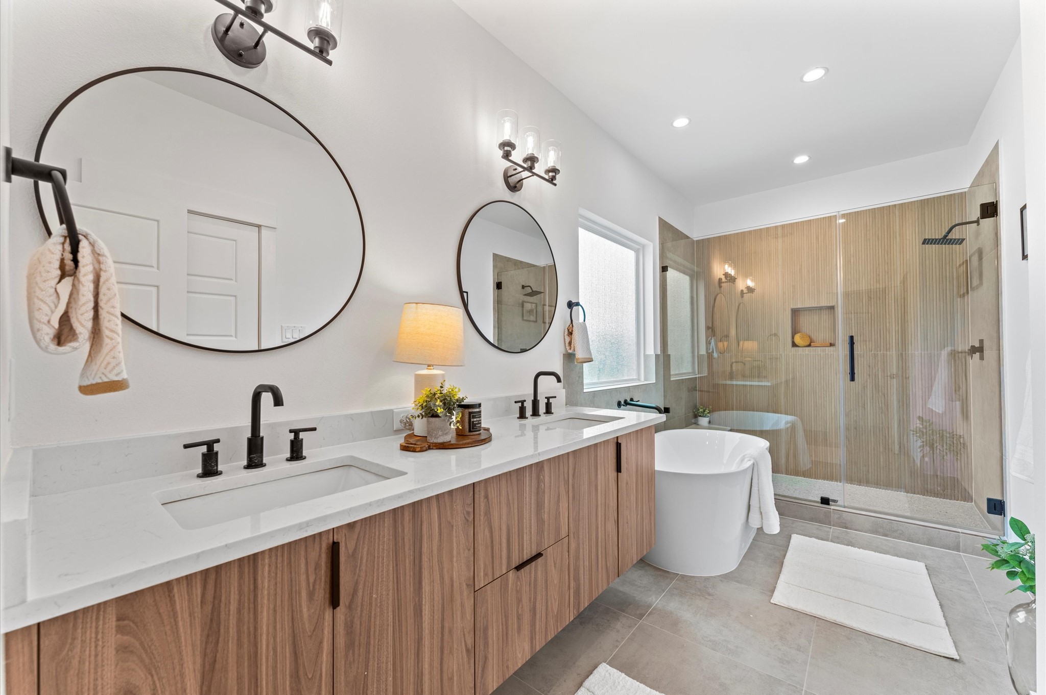 This luxurious primary bathroom blends modern elegance with spa-like comfort, featuring a spacious layout and contemporary selections throughout. A sleek double vanity with minimalist cabinetry and quartz countertops offers ample storage and style, while the glass-enclosed shower includes a built-in bench for added relaxation and convenience. The centerpiece is a sculptural freestanding soaking tub, perfectly positioned to invite unwinding after a long day.