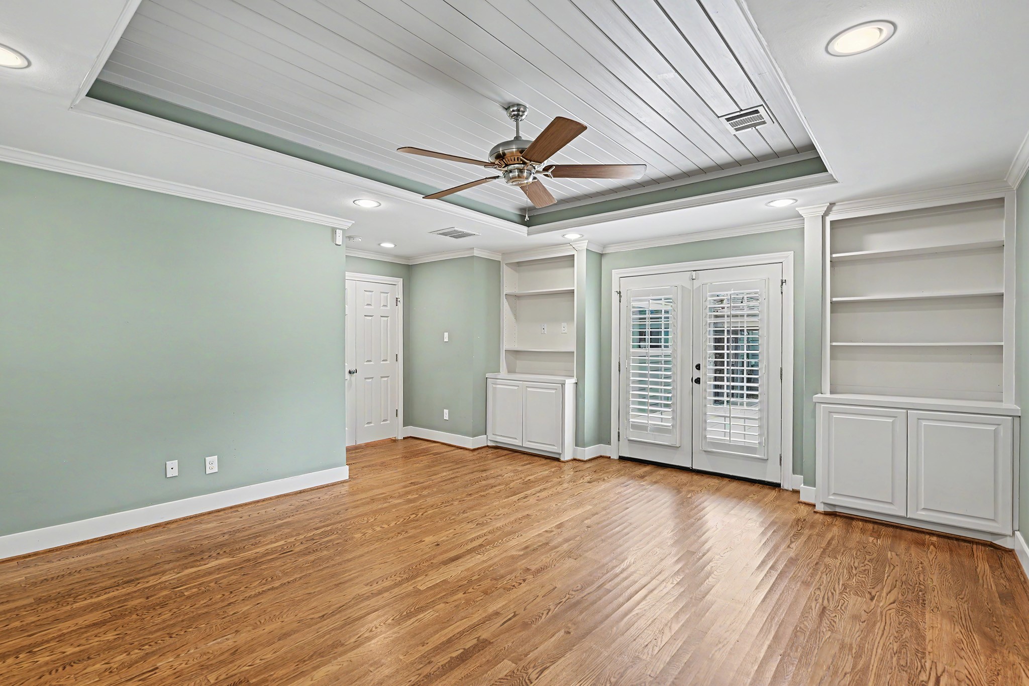 The spacious primary suite offers 3 walk-in closets, an ensuite bath, hardwood floors, built-in cabinetry and shelving, and French doors opening onto the back deck.