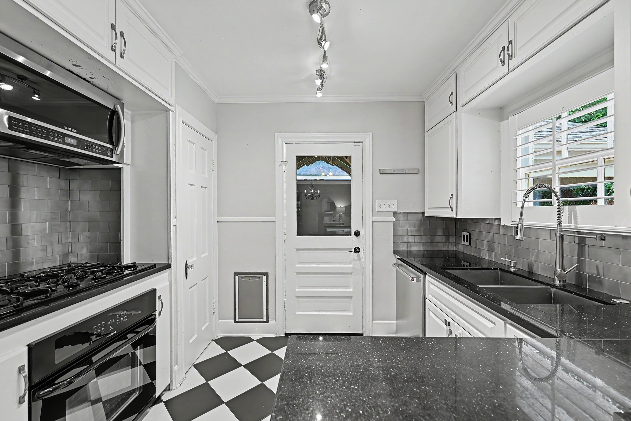 Classic black-and-white tile flooring pairs with a modern backsplash and updated appliances, including a gas cooktop and large sink. Back door leads to the covered deck with fan and porch swing.
