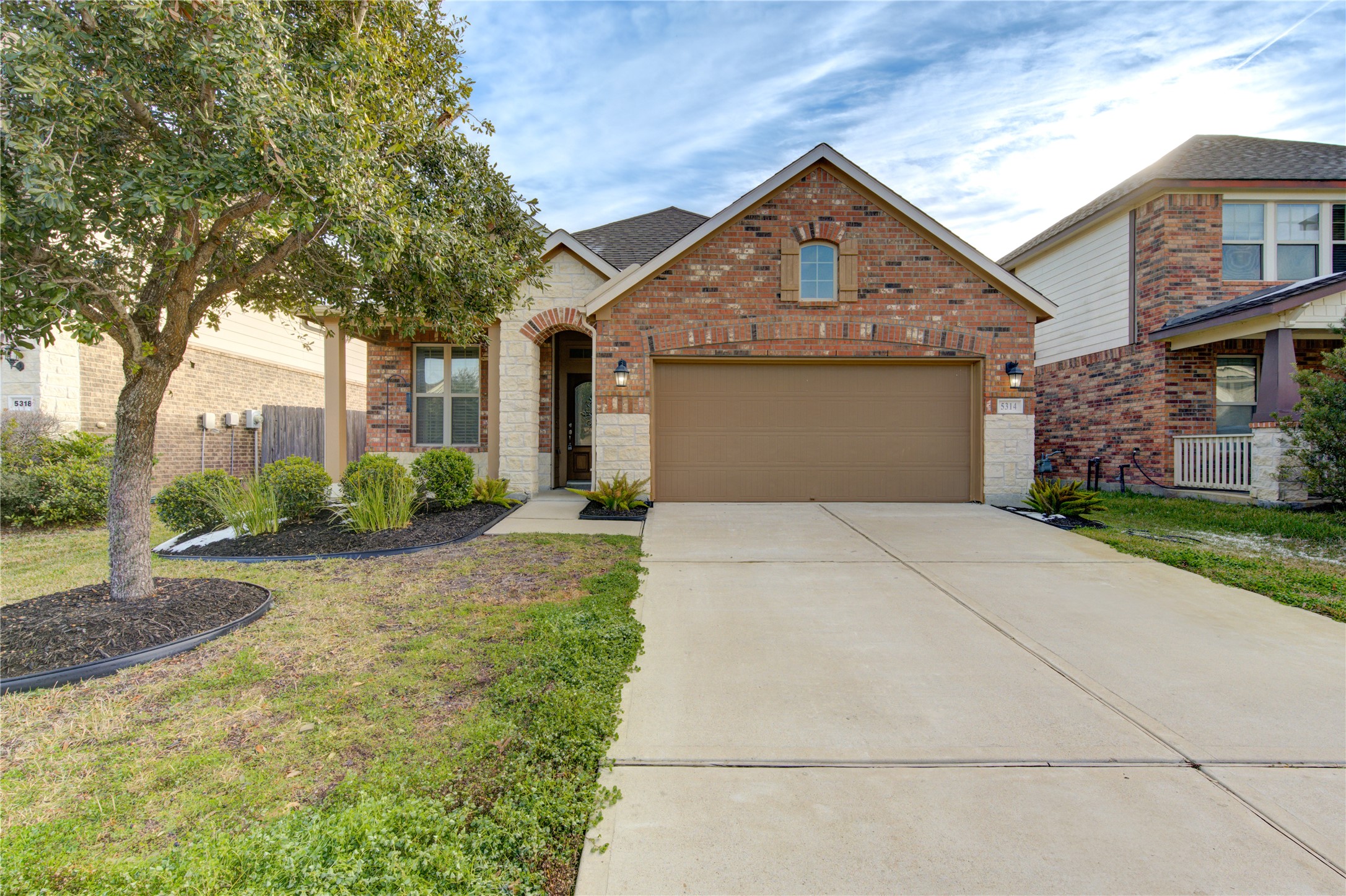 This charming brick home features a welcoming front porch, well-maintained landscaping, and a two-car garage. The arched entryway adds character, and the driveway offers ample parking.