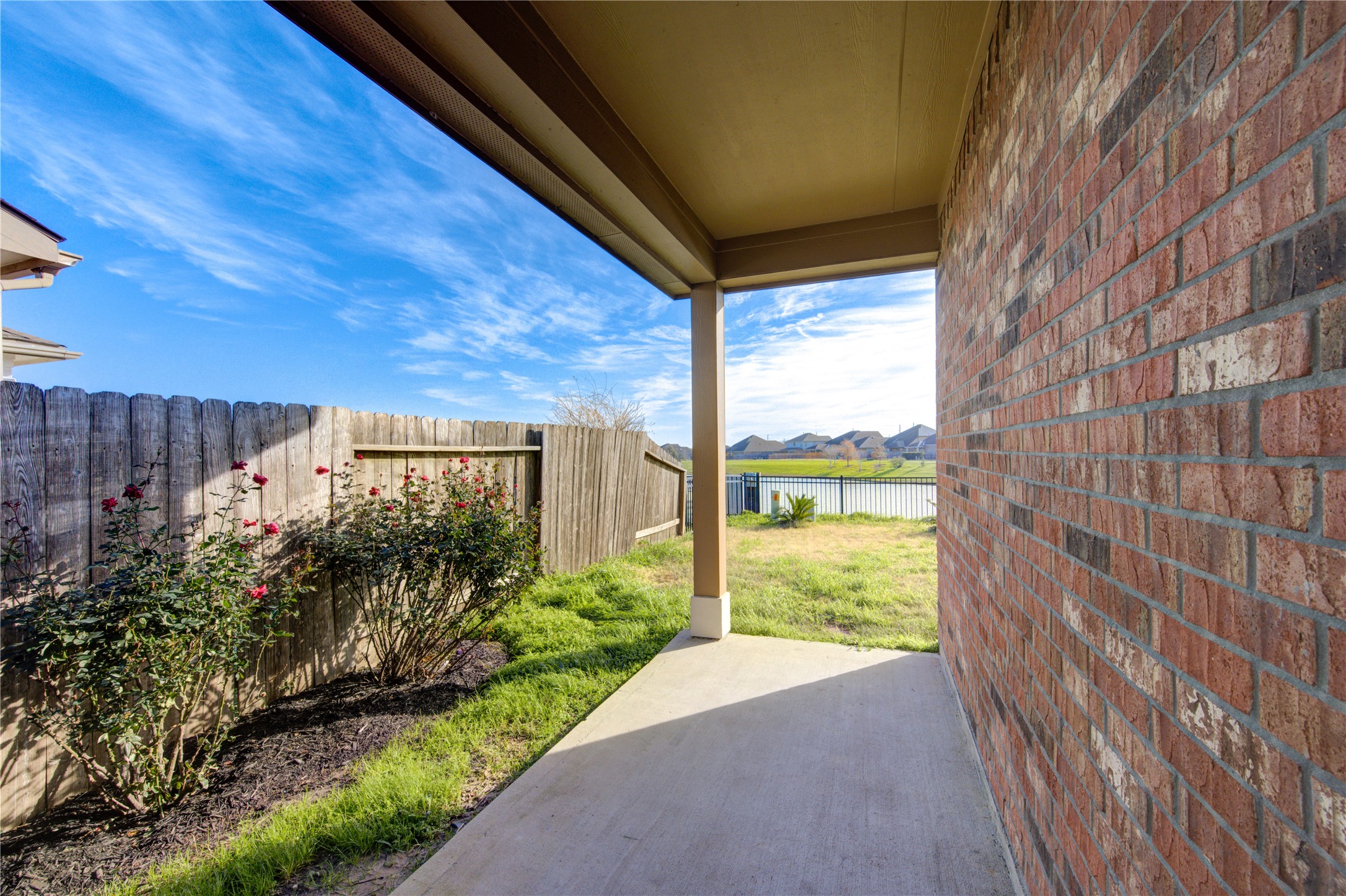 This photo showcases a serene neighborhood with a wide, calm lake and a fountain, surrounded by well-maintained lawns and houses. The sky is bright and clear, offering a peaceful and inviting atmosphere.