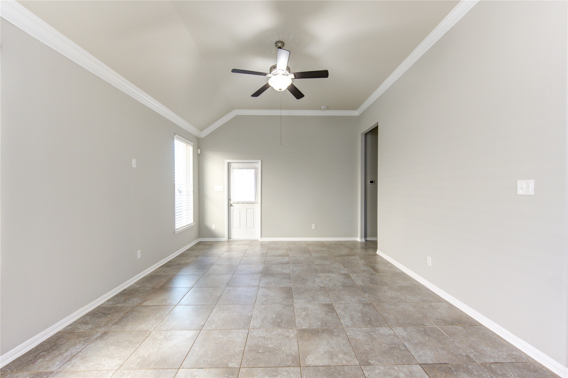 This photo showcases a spacious open-concept living area with a modern kitchen featuring dark cabinets, a large island, and stainless steel appliances. The room is bright with natural light from multiple windows, and the tile flooring offers a clean, contemporary feel. The ceiling fan and neutral color palette add to the inviting atmosphere.