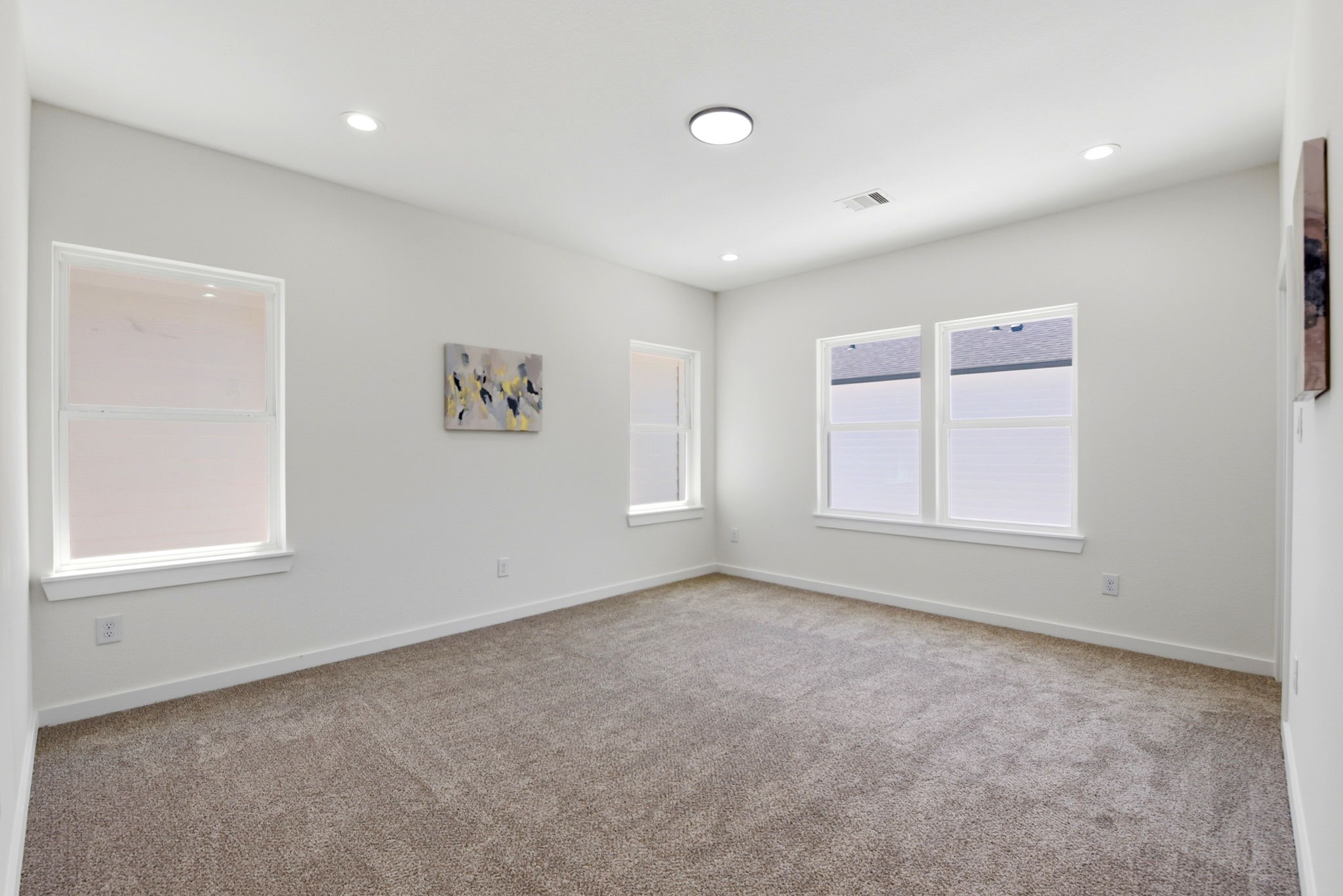 Bright and spacious primary bedroom with neutral walls and cozy carpeting, featuring recessed lighting and large windows for ample natural light.