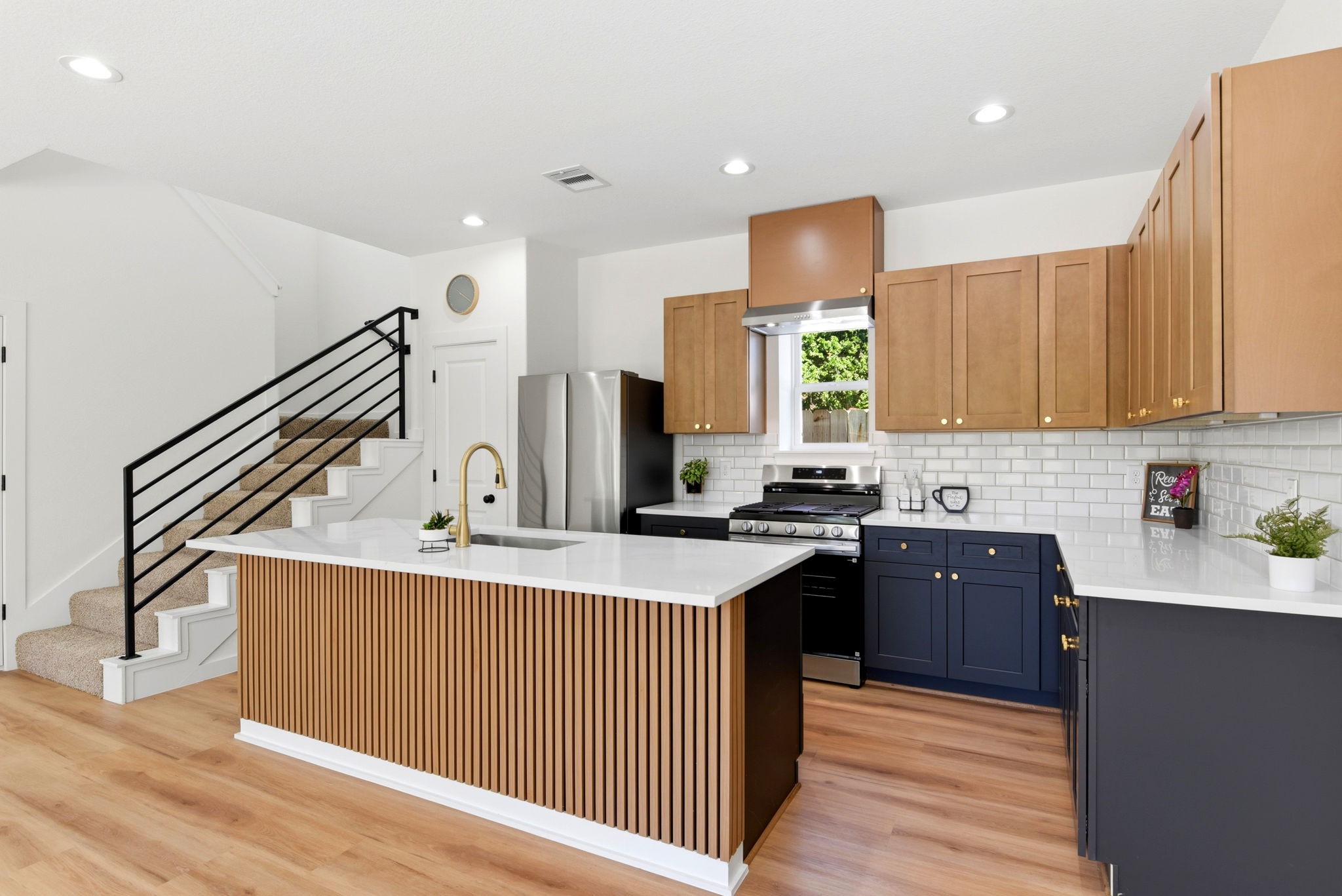 This kitchen features a modern design with light wood cabinetry, a sleek island with vertical paneling, and stainless steel appliances.