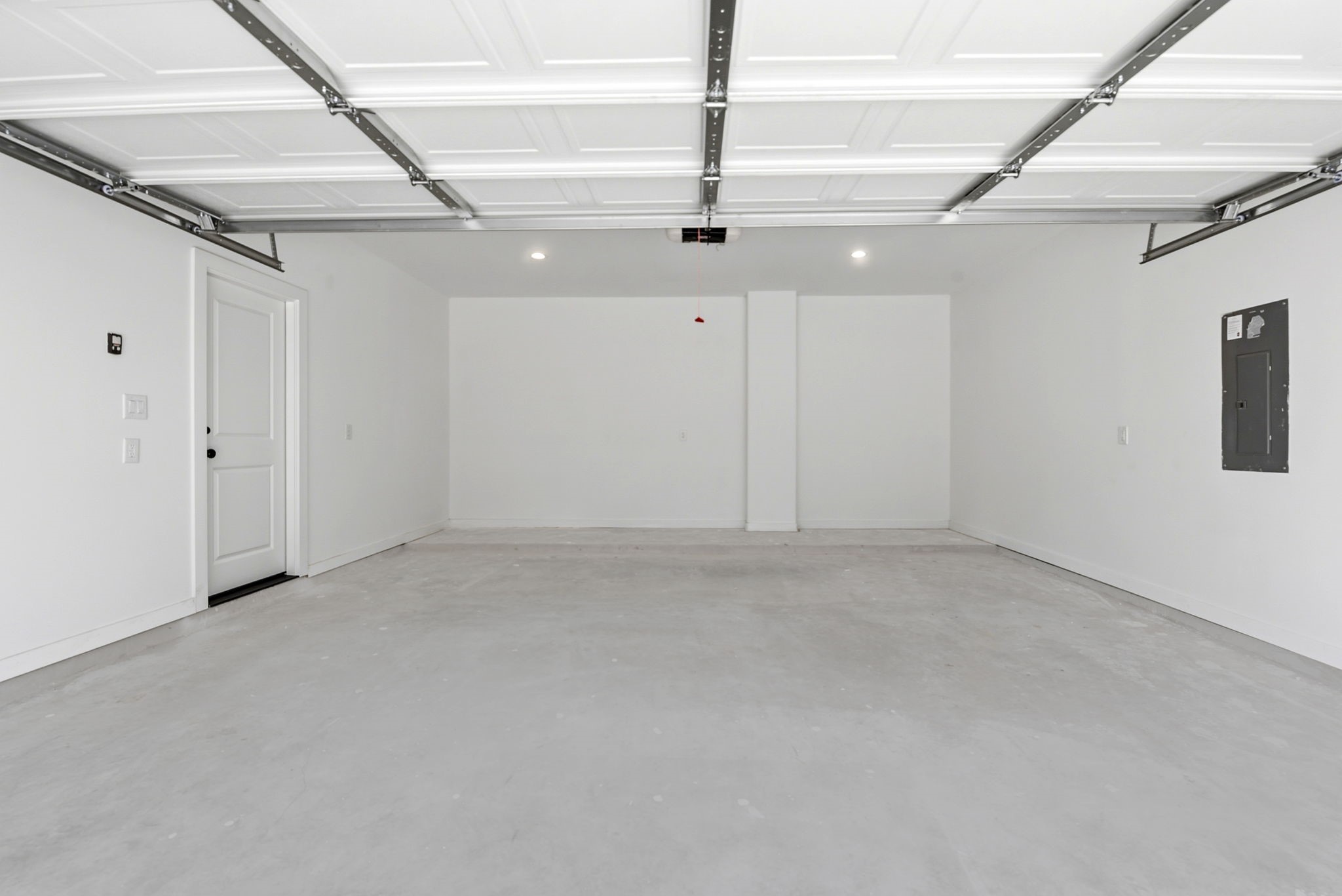 Spacious, clean garage with a white interior, overhead lighting. Plenty of space for additional storage.