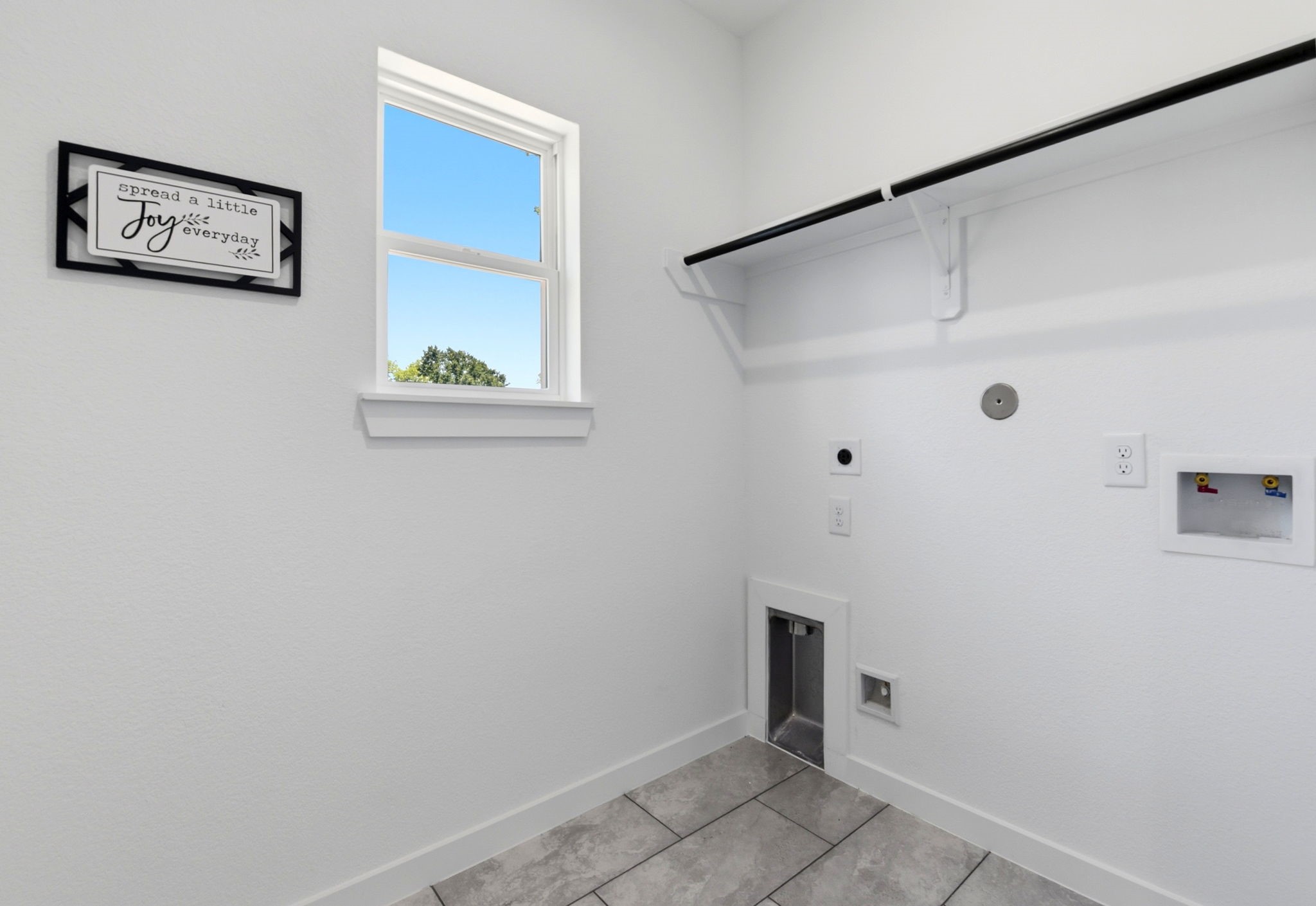 Bright, functional laundry room with a small window, tile flooring, and wall storage for organization. Gas and electrical connections available.