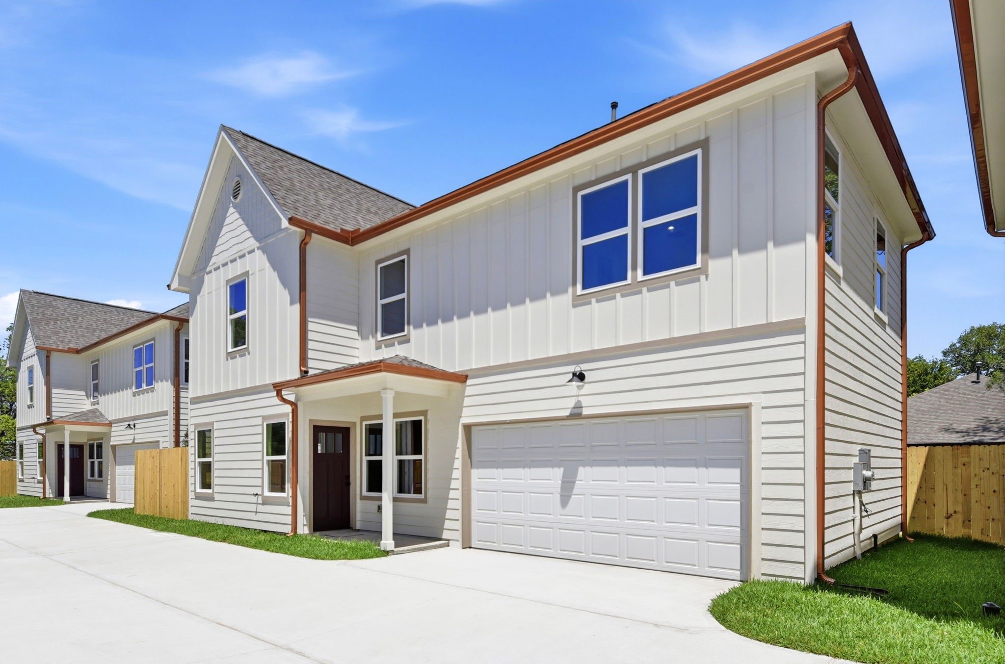 Modern, two-story home with a clean, light exterior and a double garage. The house features a gable roof, gutters and large windows, enhancing natural light.