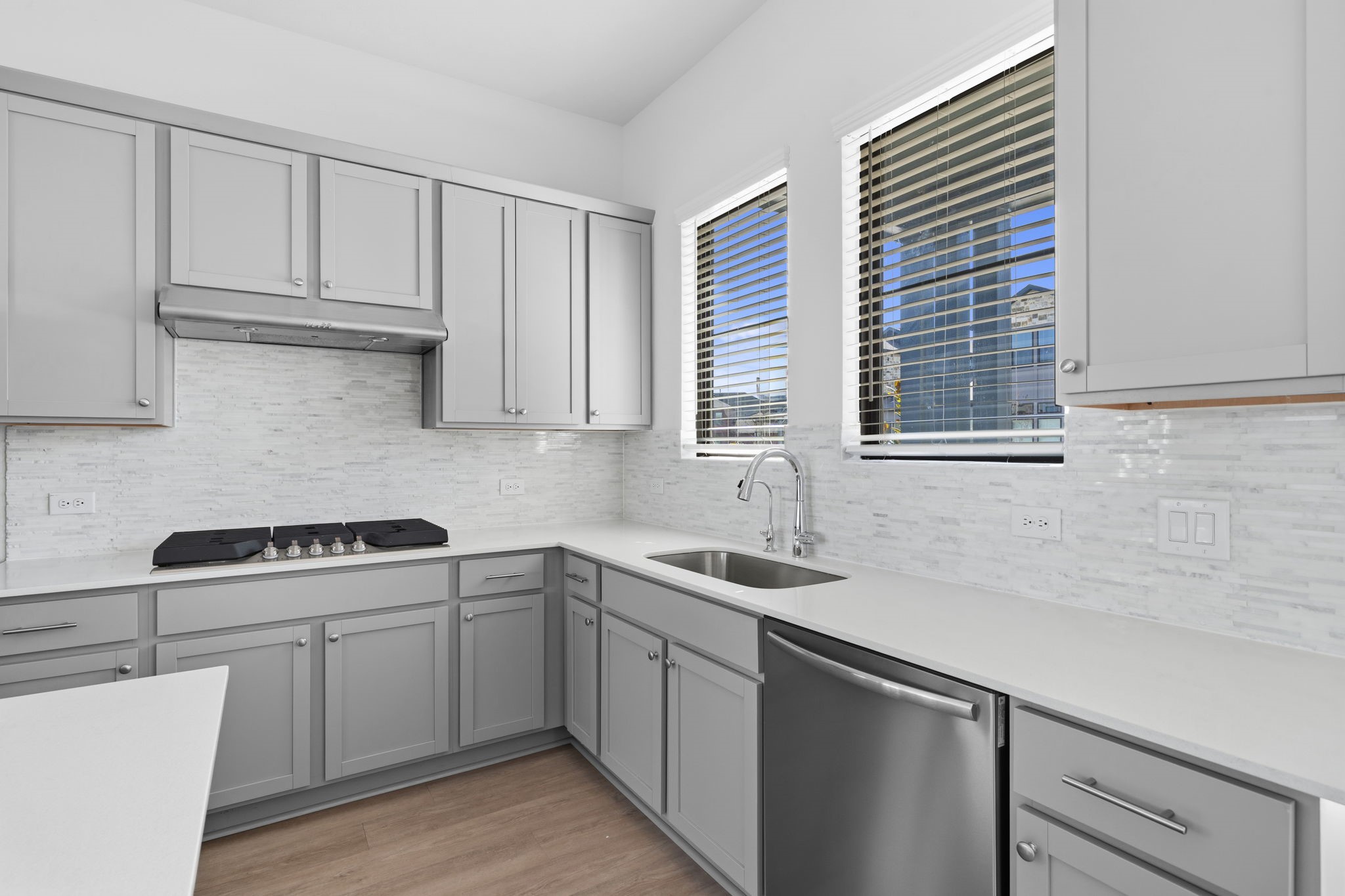 Welcome to a kitchen designed to feel bright, polished, and effortlessly functional. Soft grey cabinetry pairs beautifully with the light backsplash and quartz countertops, while the windows above the sink bring in natural light and create a refreshing connection to the outdoors.