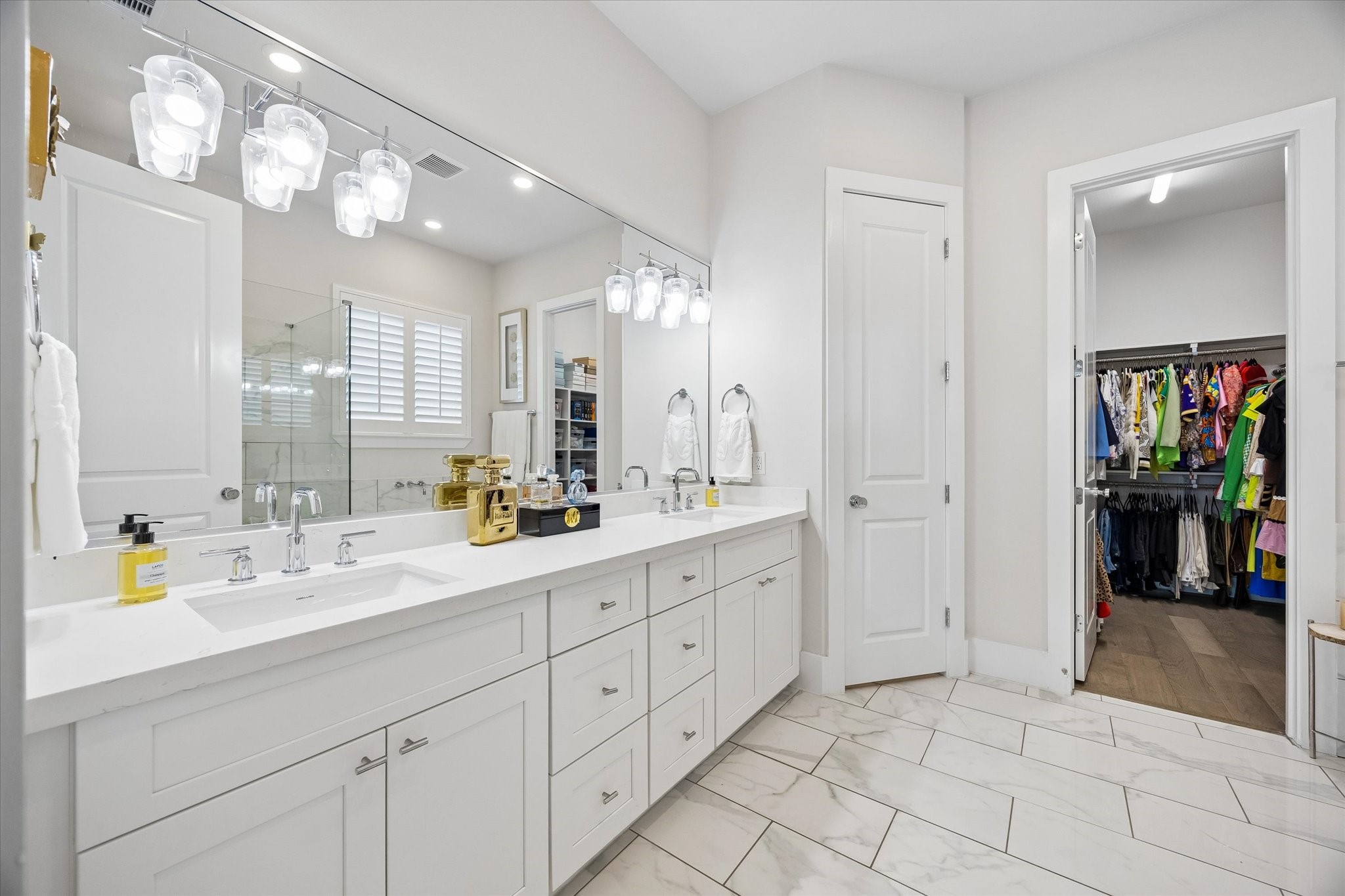 The spa-like primary ensuite feels crisp and luxurious with a long dual-sink vanity, bright designer lighting, beautiful tile flooring, and a large walk-in closet that keeps everything close and organized.