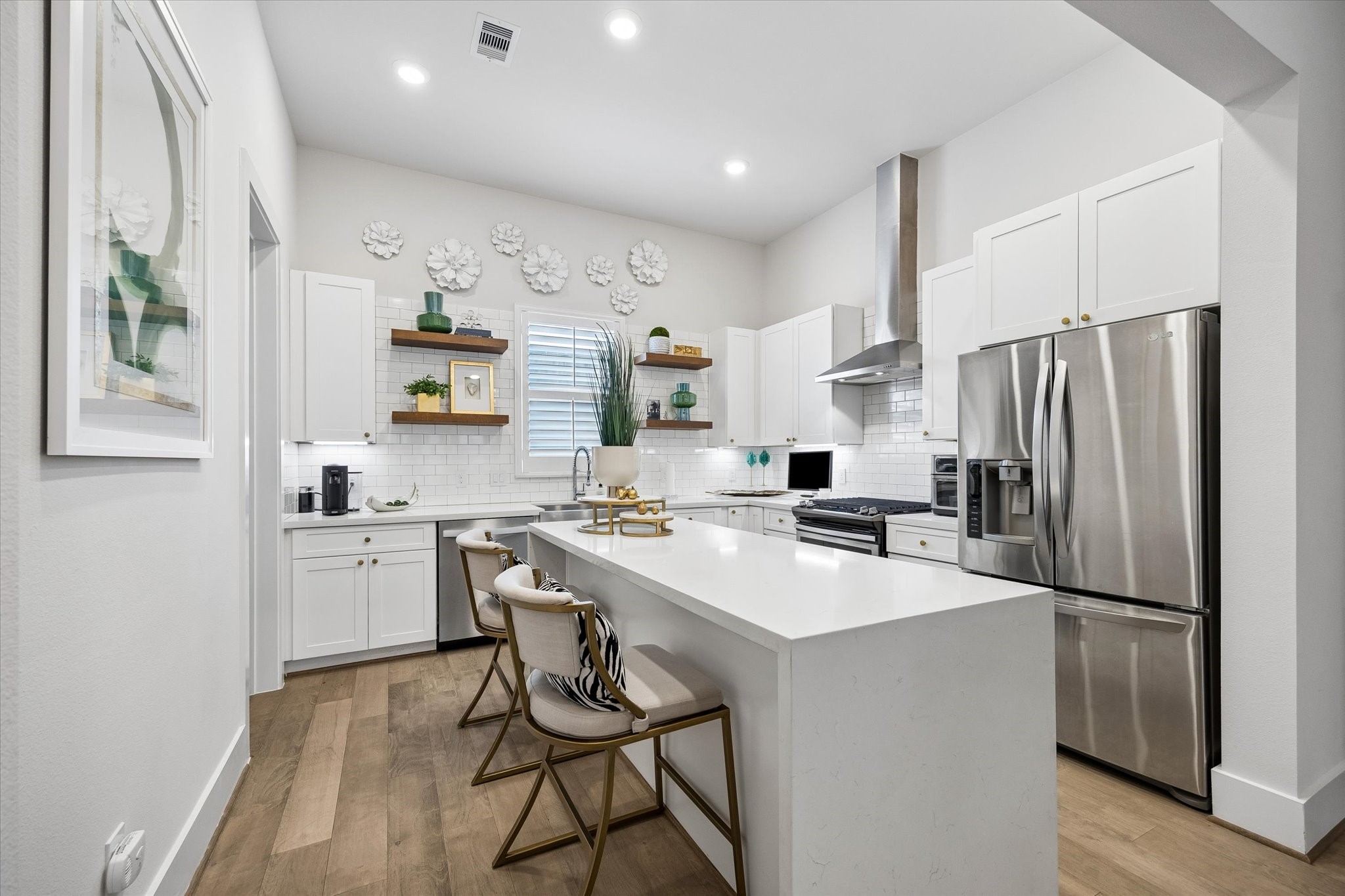 This stylish island kitchen brings the wow factor with quartz countertops, a waterfall island with bar seating, stainless-steel appliances, a sleek hood vent, open shelving, and crisp modern cabinetry.