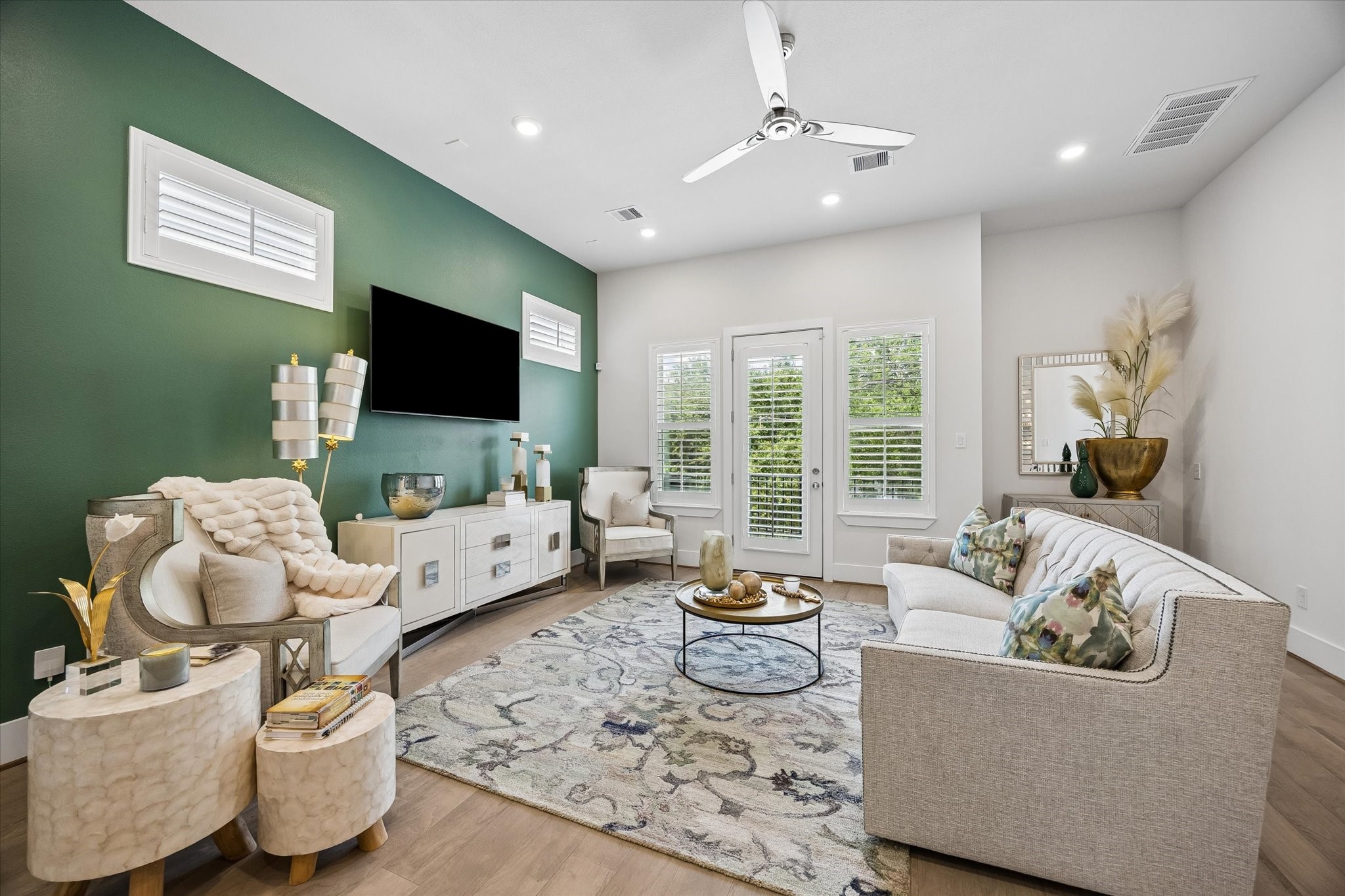 The main-floor living area feels bright and inviting with engineered wood flooring, recessed lighting, wood shuttered windows, balcony access, and a bold designer accent wall that gives the space a stylish, memorable feel.