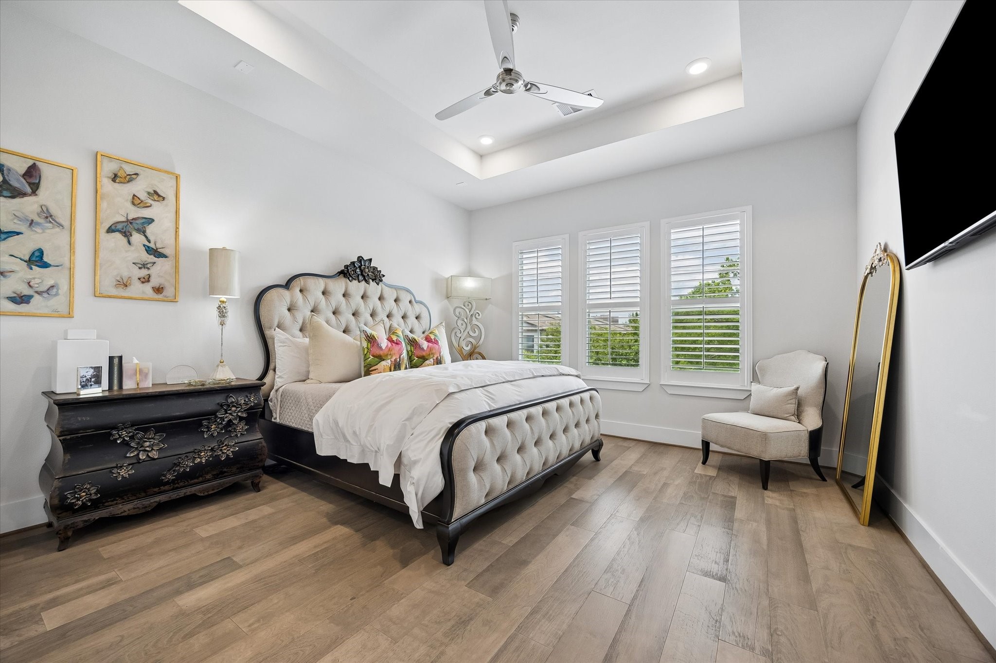 This posh owners retreat offers a peaceful place to rest and recharge with warm engineered wood flooring, wood shuttered windows, soft neutral paint, a raised tray ceiling, recessed lighting, and a cooling ceiling fan.