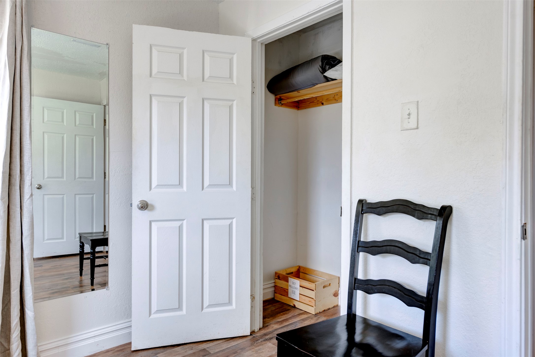 Bedroom closet detail showing white six-panel door, natural wood upper shelf with hanging rod, and hardwood-style flooring throughout.